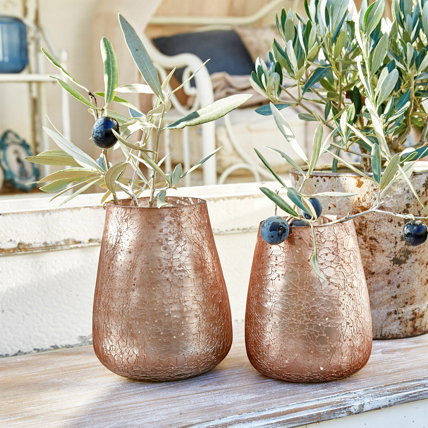Twee koperen glazen vazen met gebarsten textuur en olijftakken op houten tafel