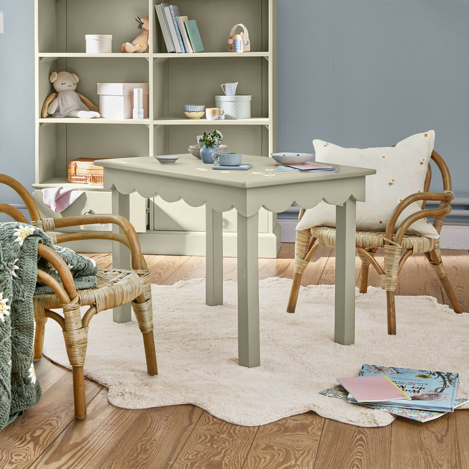 Grijze houten tafel met golvende rand op lichte vloerkleed in gezellige kinderkamer met rotan stoelen