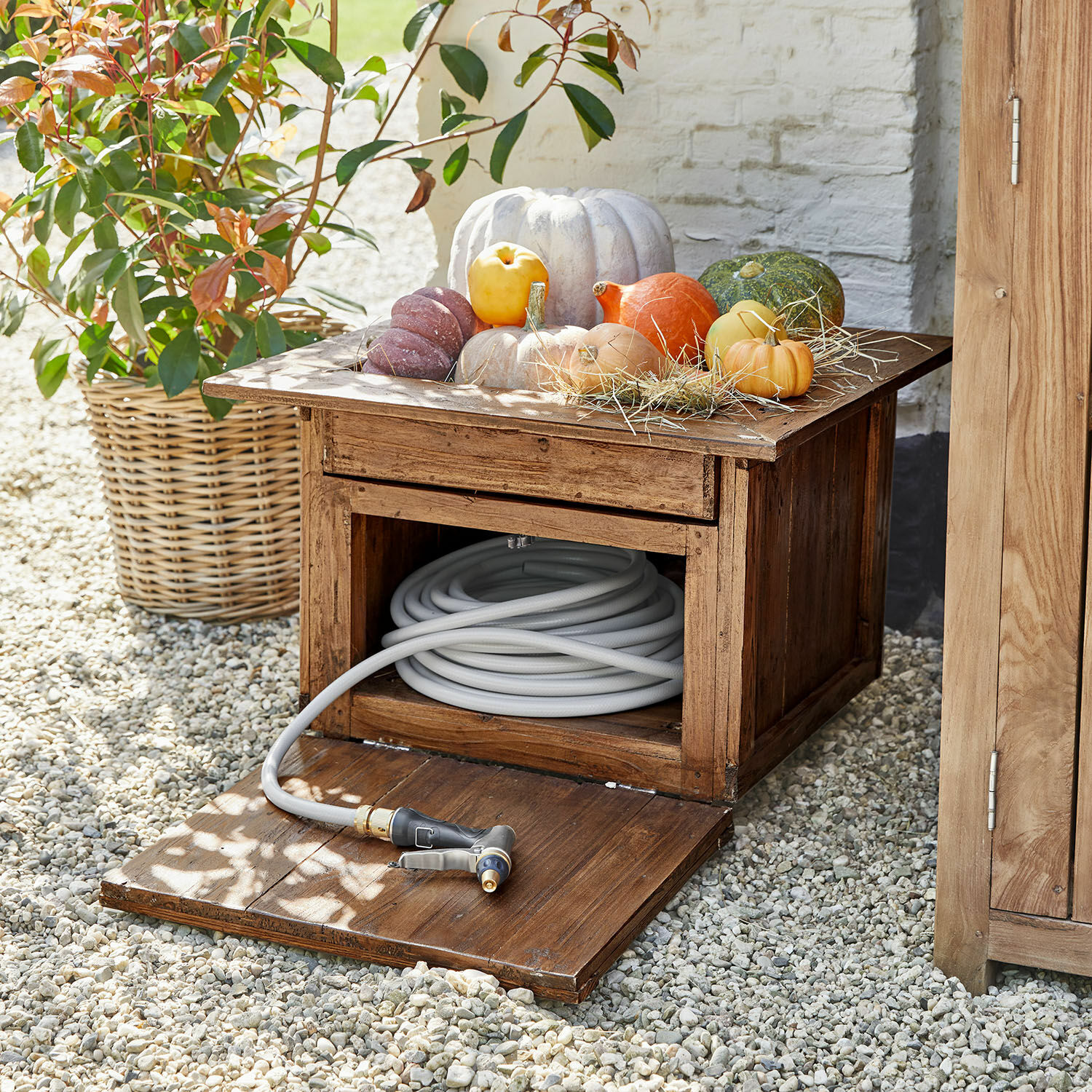 Houten tuinkast met grijze tuinslang en decoratieve pompoenen bovenop