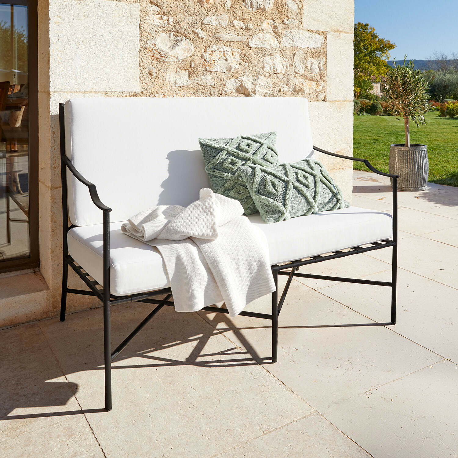 Bank Vexford Witte metalen tuinbank met zachte kussens en groene sierkussens op zonnig terras