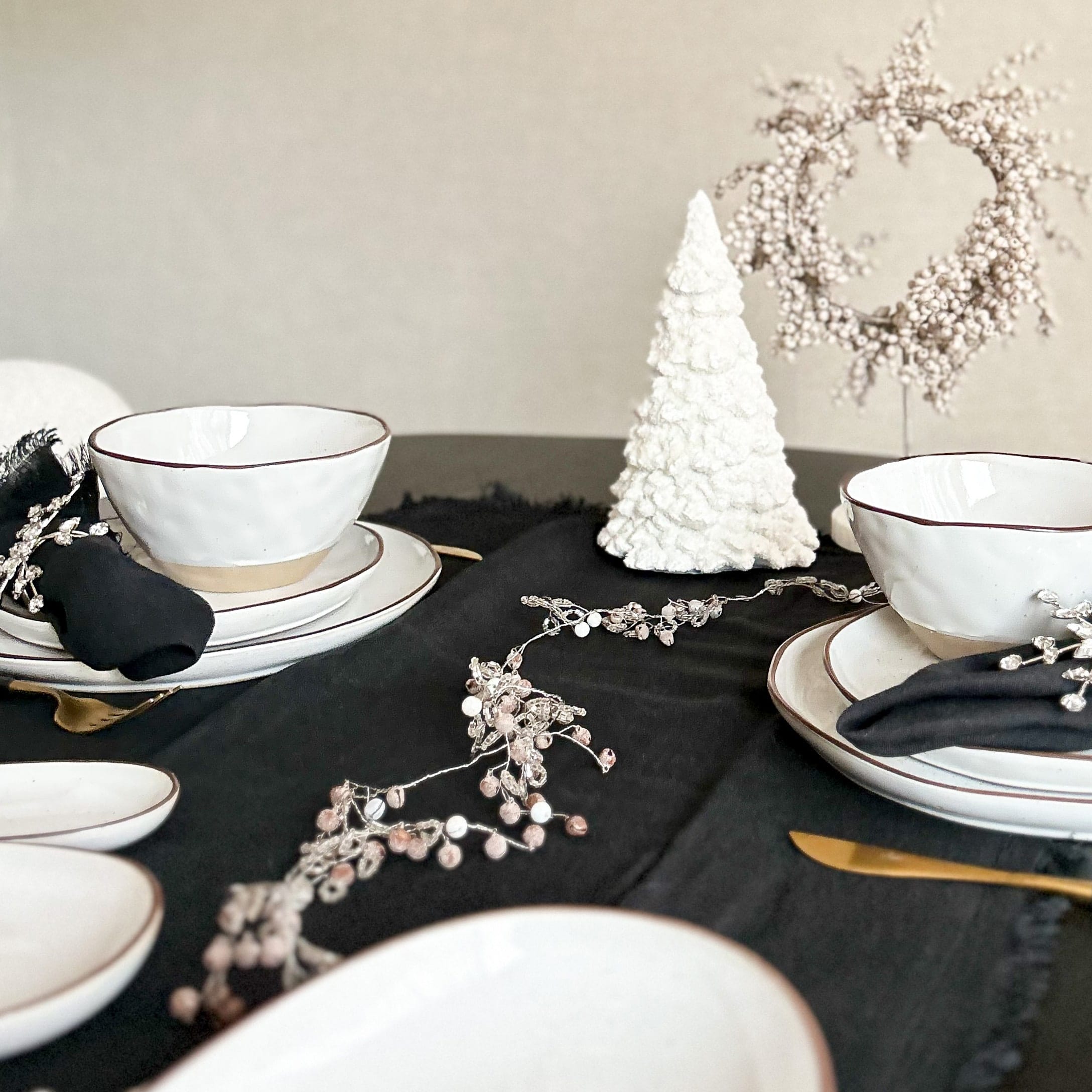 Witte keramische servies met bruine rand op zwart tafelkleed met kerstdecoratie