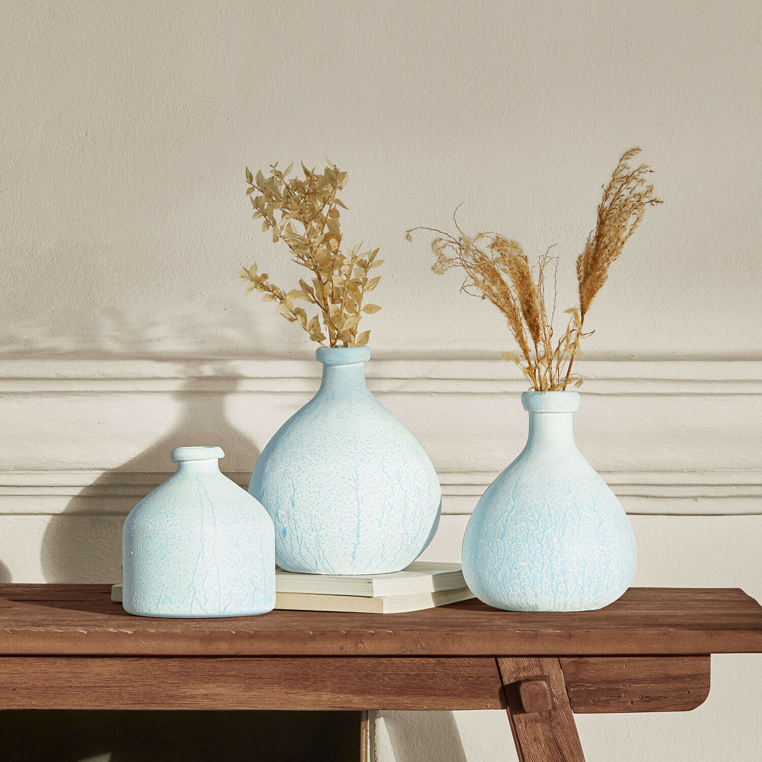 Set van drie lichtblauwe keramische vazen met gedroogde planten op houten tafel voor interieurdecoratie