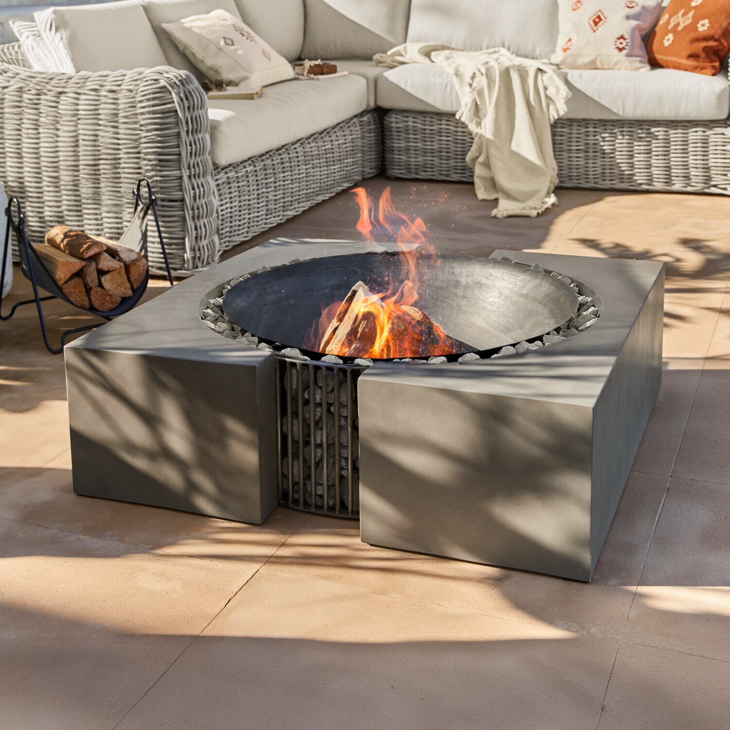Moderne vuurkorf van zwart metaal met stenen op terras bij rotan bank met kussens