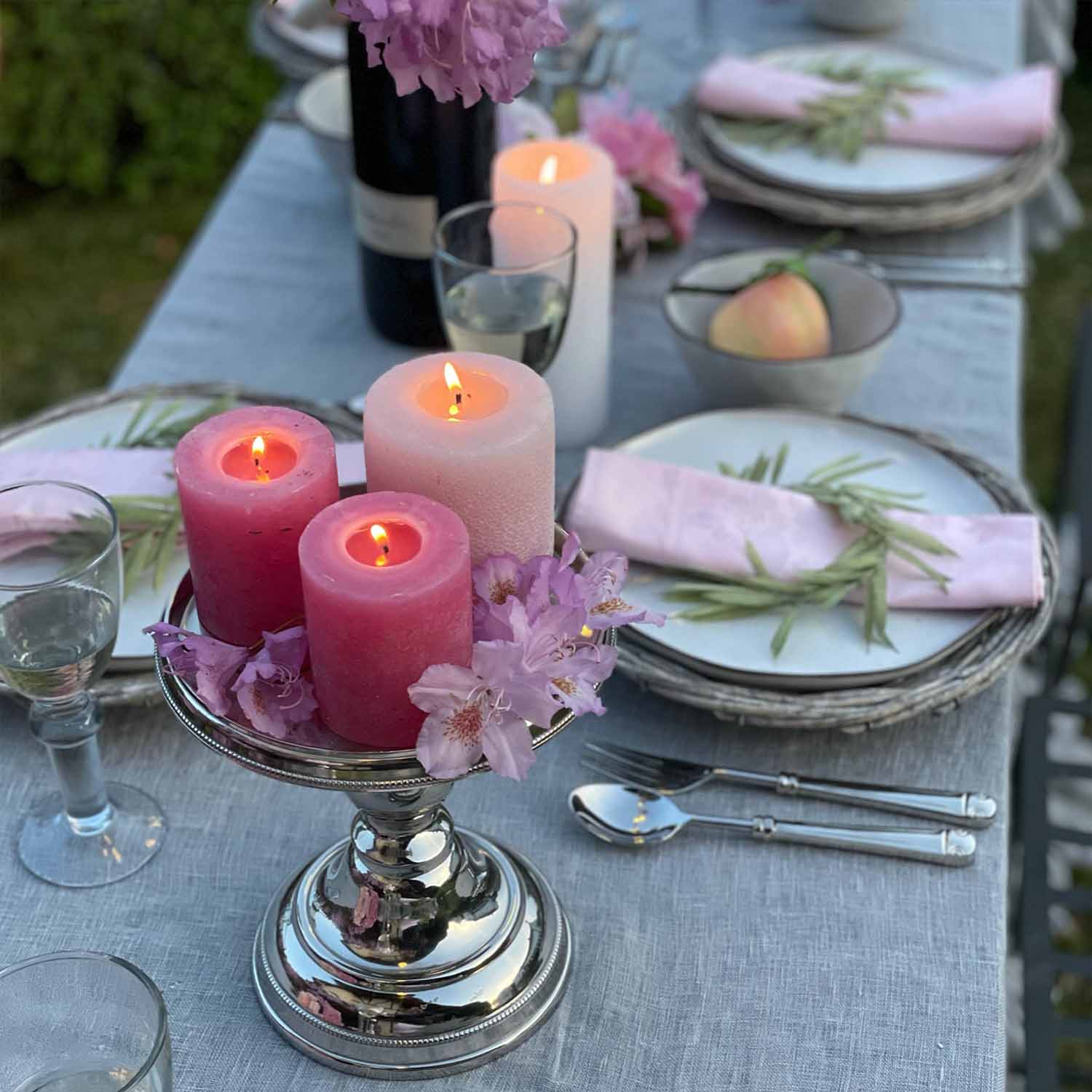 Zilveren kandelaar met drie brandende roze en witte kaarsen op een grijze tafelkleed met bloemen