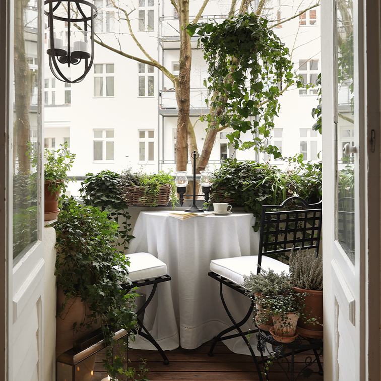 Gezellig balkon met witte tafel, zwarte stoelen en groene planten, perfect om te ontspannen.