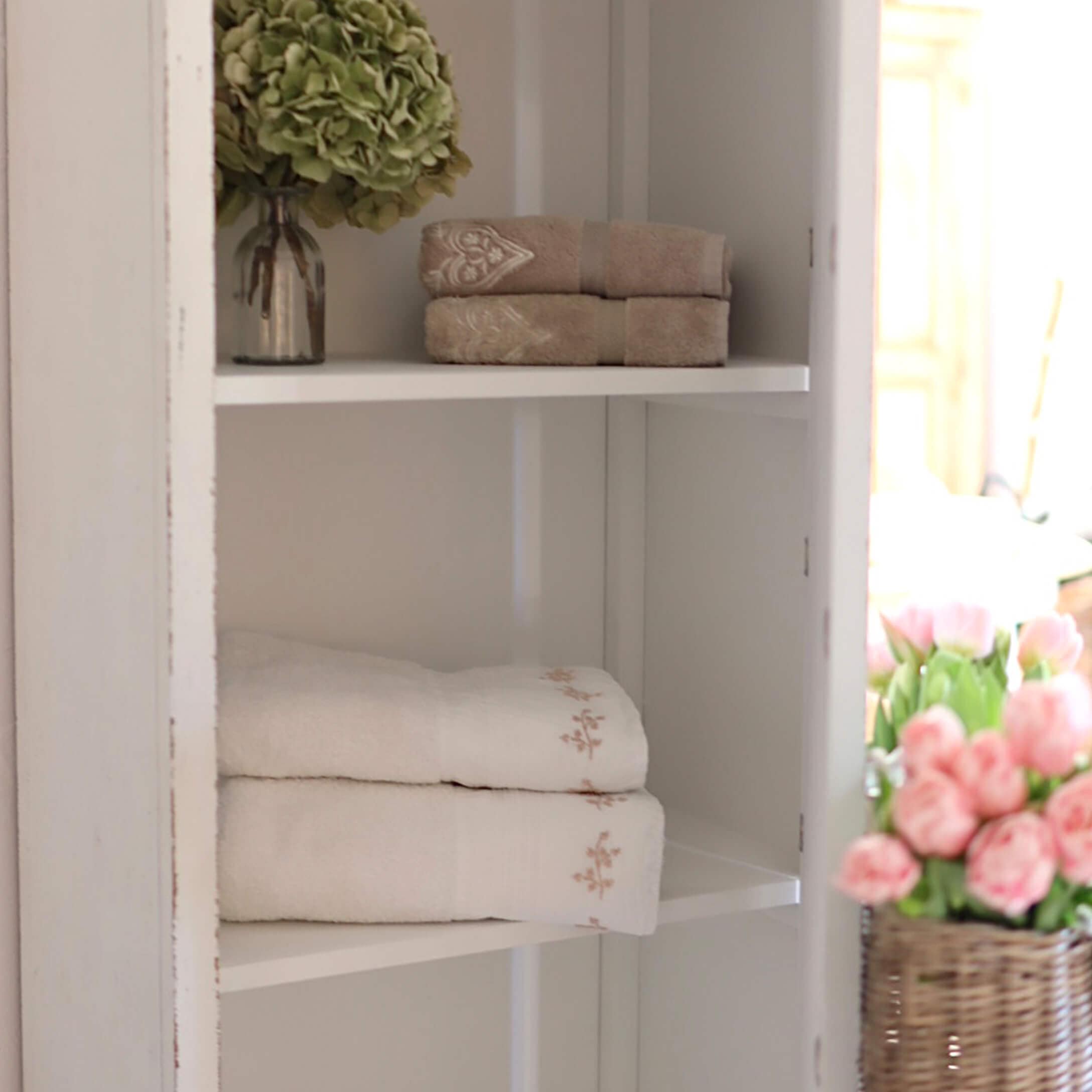 Zachte katoenen handdoeken in beige en wit met fijne borduursels op een witte plank