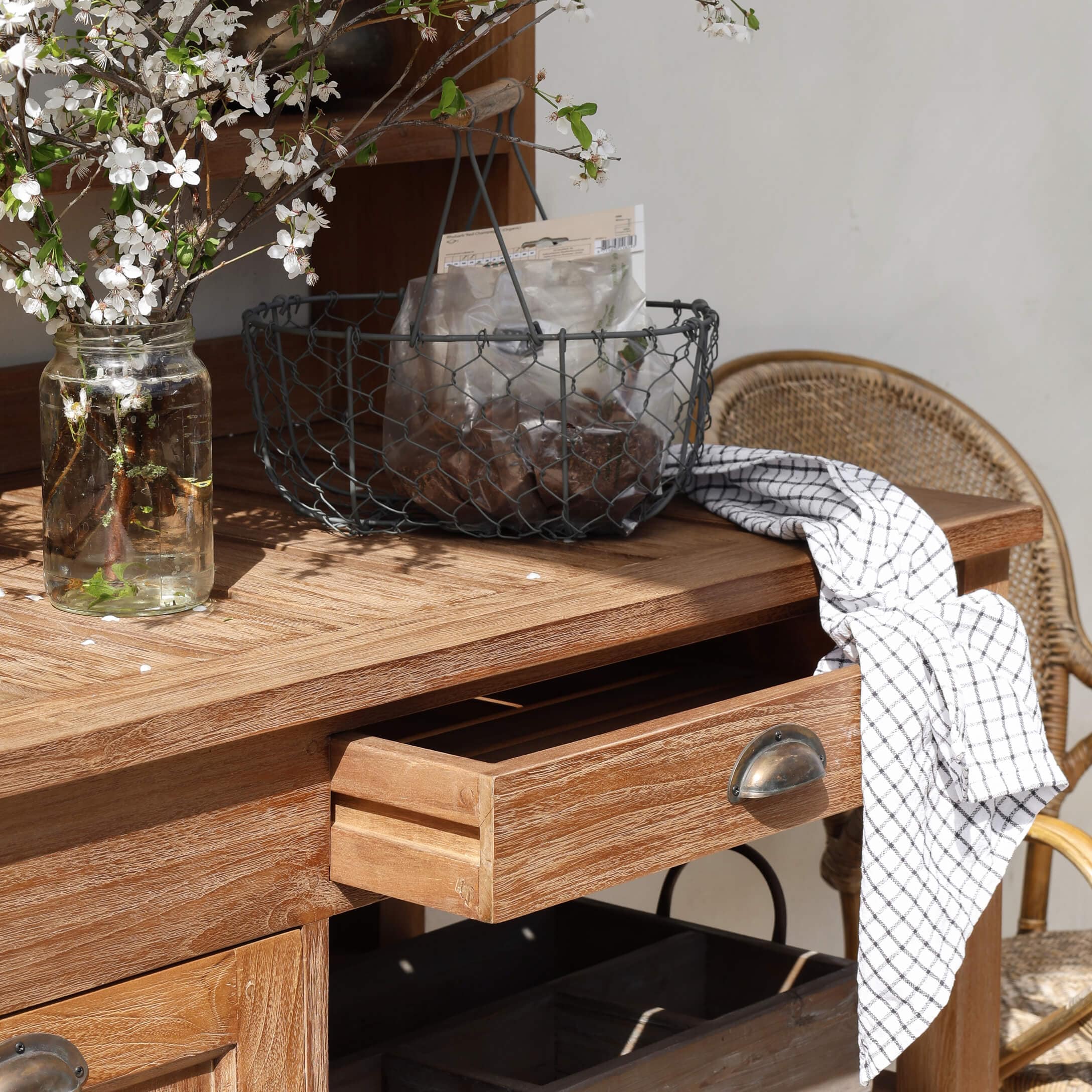 Houten tafel met open lade, metalen mand en wit geruit doek op het blad