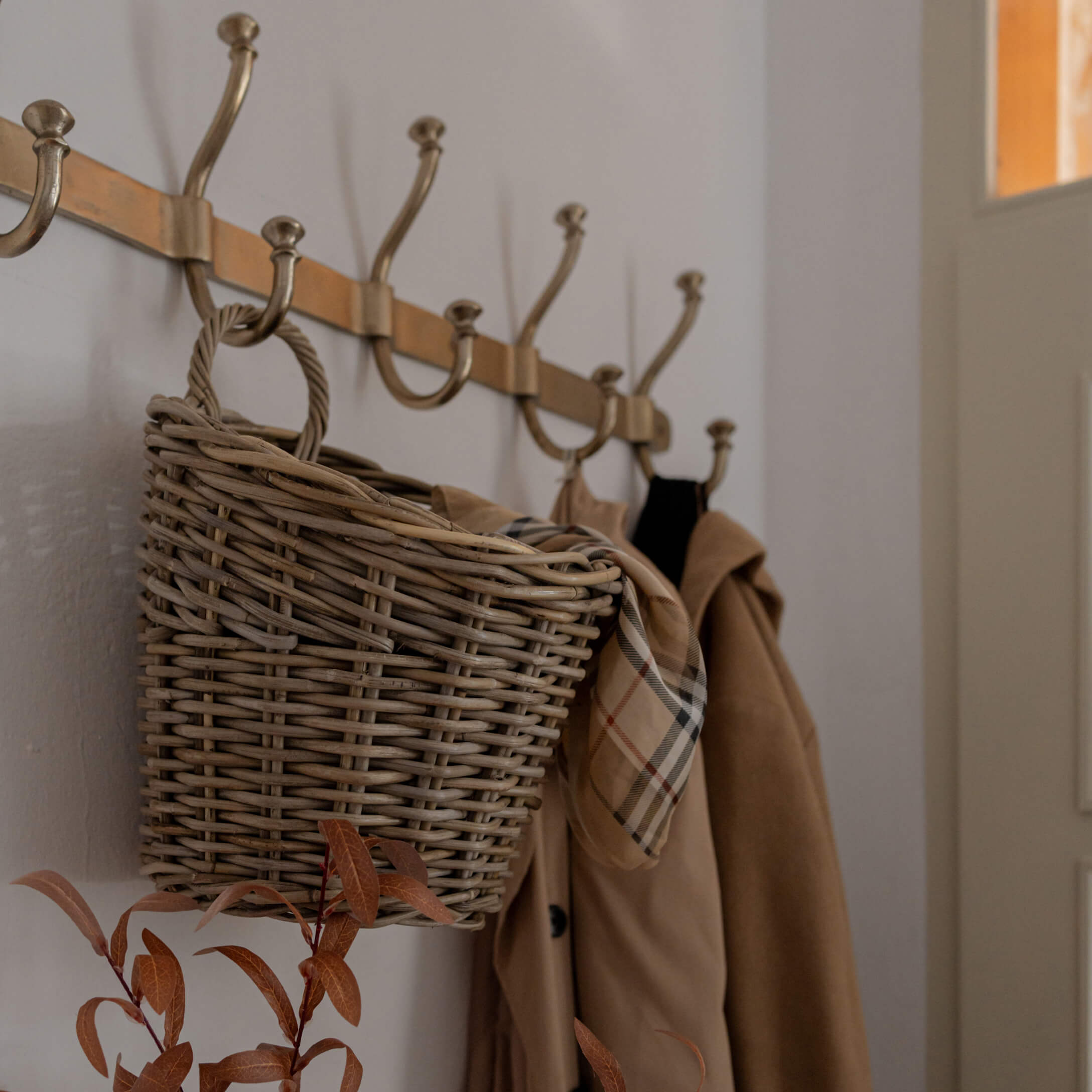 Rieten mand hangend aan messing kapstok met beige jas en geruite sjaal