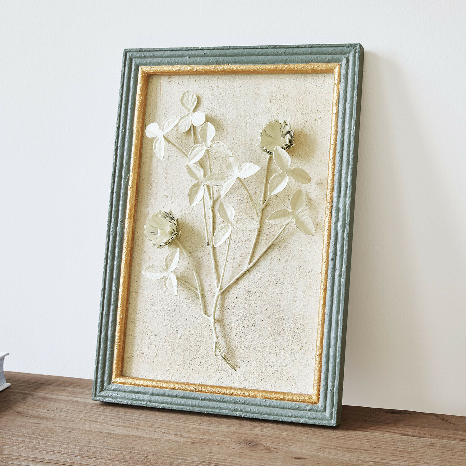 Decoratief schilderij met bloemenreliëf in groen-gouden lijst op houten tafel