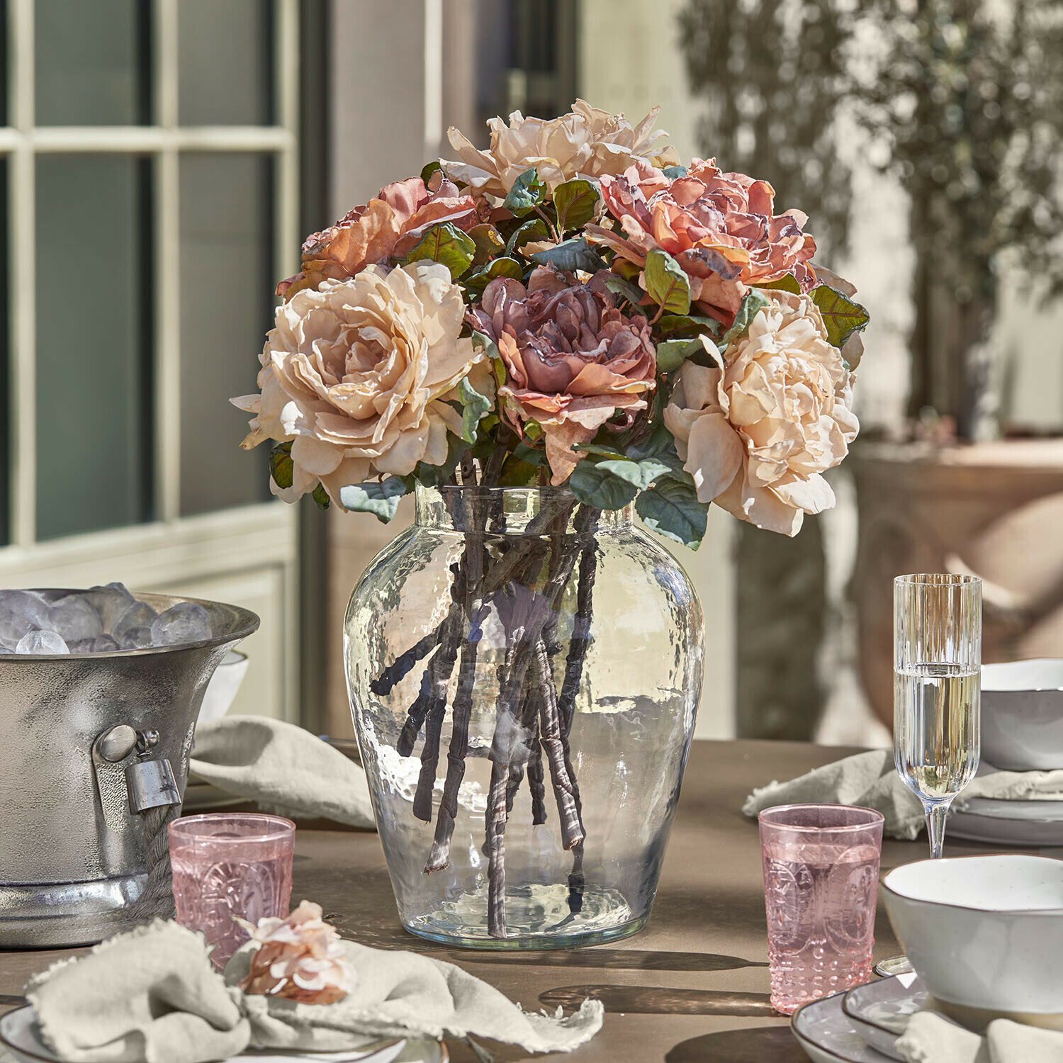 Vaas Lunaras Boeket beige en roze rozen in een doorzichtige glazen vaas op een gedekte tafel
