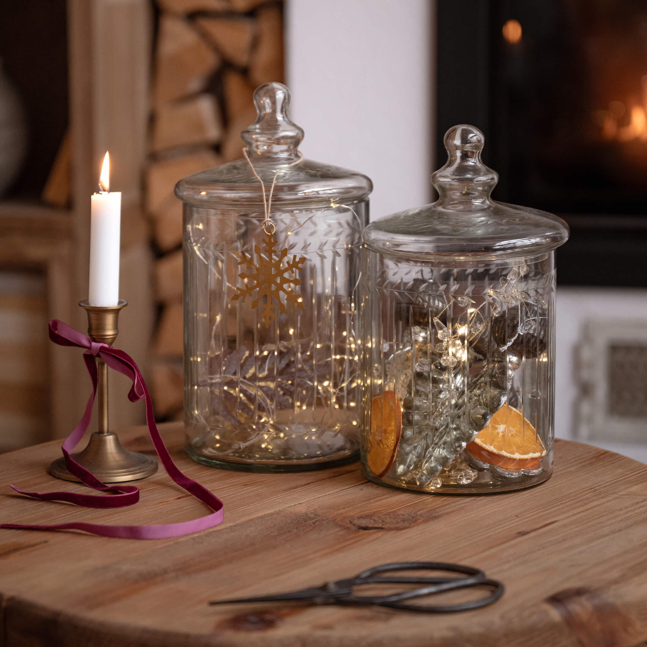 Transparante glazen potten met deksels op houten tafel, versierd met lichtjes en brandende kaars