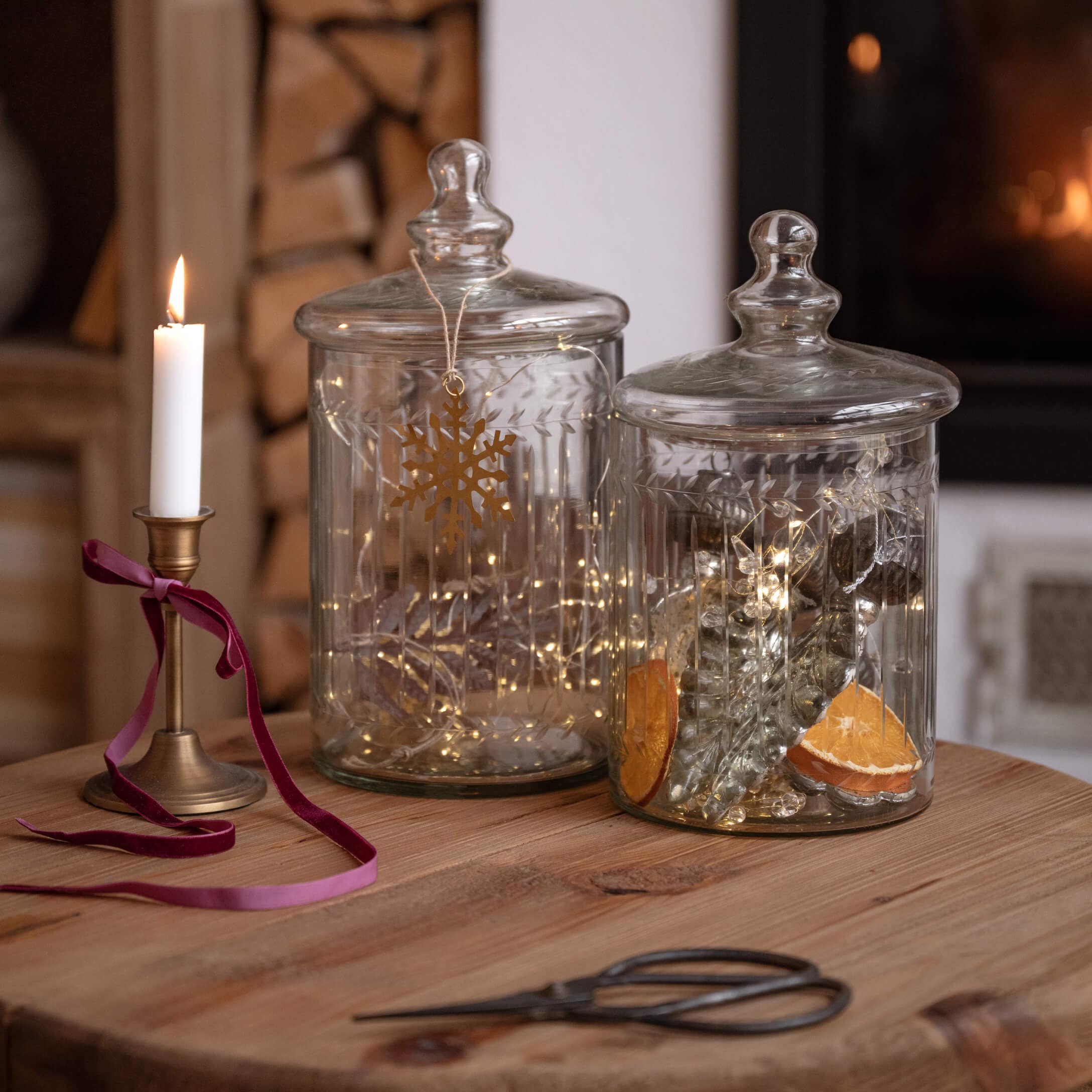 Transparante glazen potten met deksels op houten tafel, versierd met lichtjes en brandende kaars