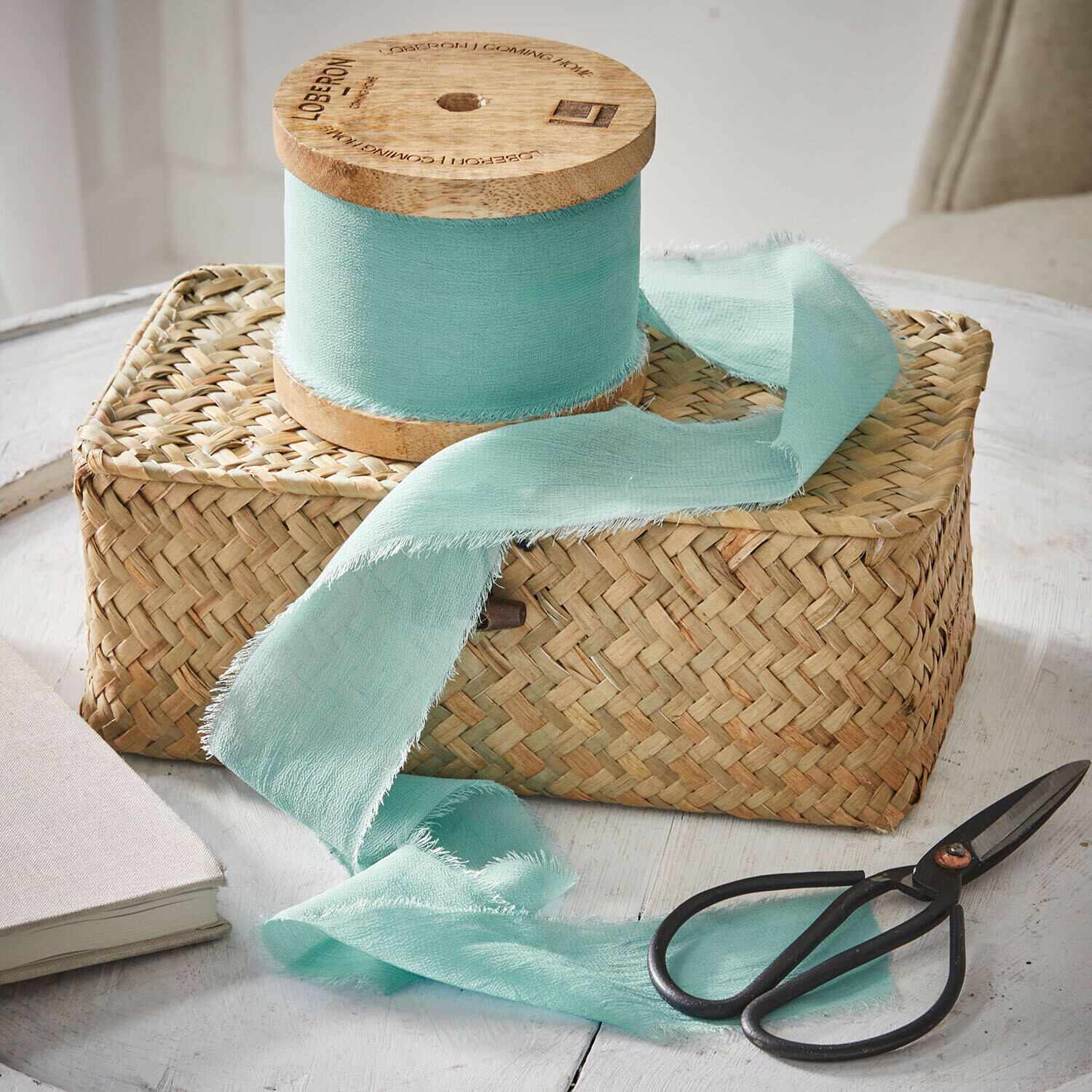 Mintgroene katoenen lint op houten klos op gevlochten mand met zwarte schaar