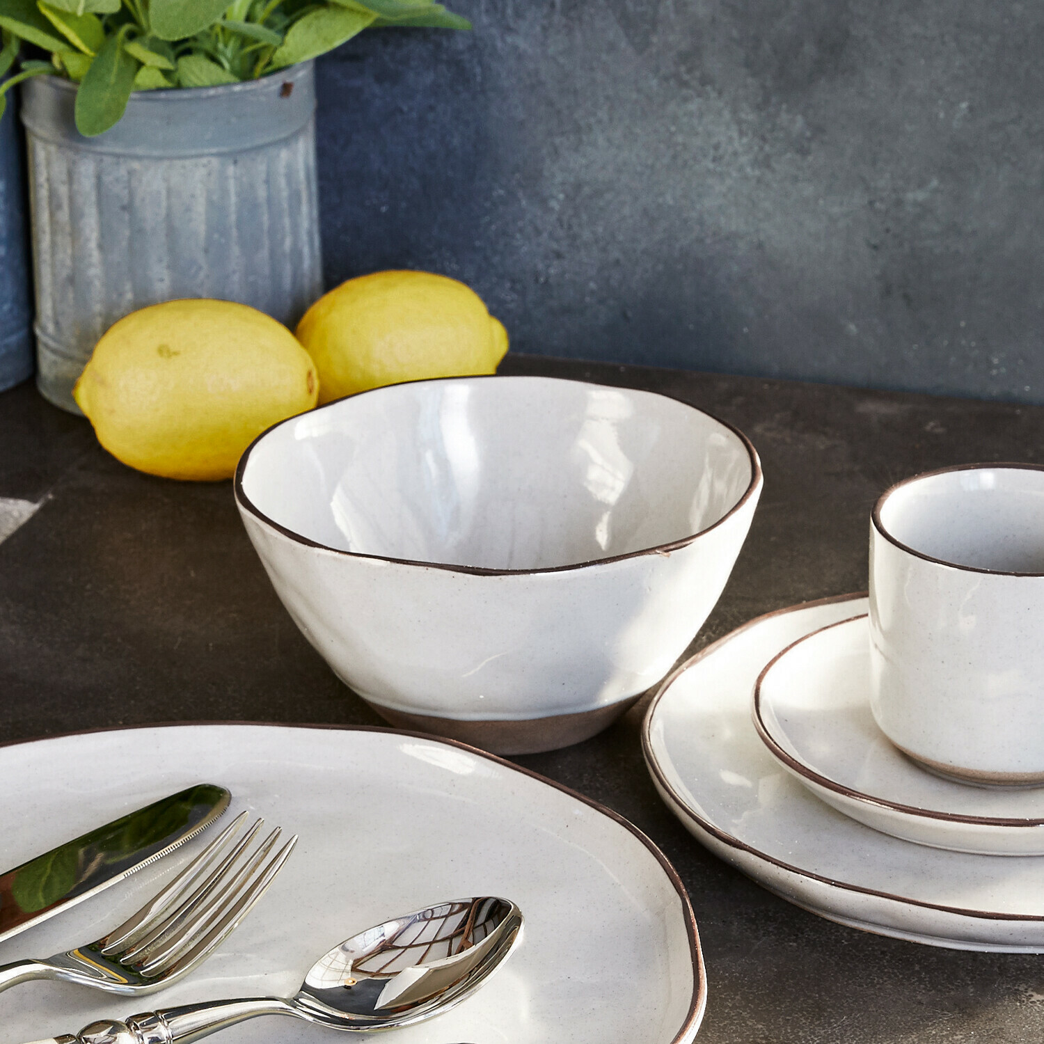 Wit keramisch servies met bruine rand op donkere keukenblad met citroenen