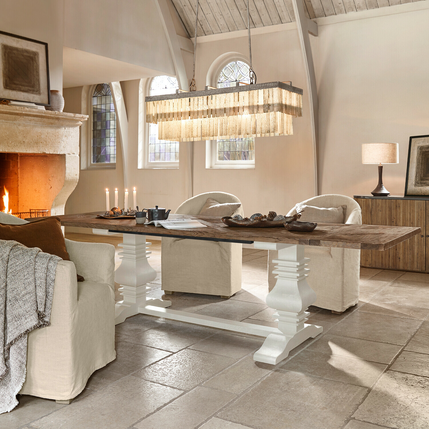 Tafel Quillancourt Grote houten tafel met witte onderstel in lichte woonkamer met open haard en beige fauteuils