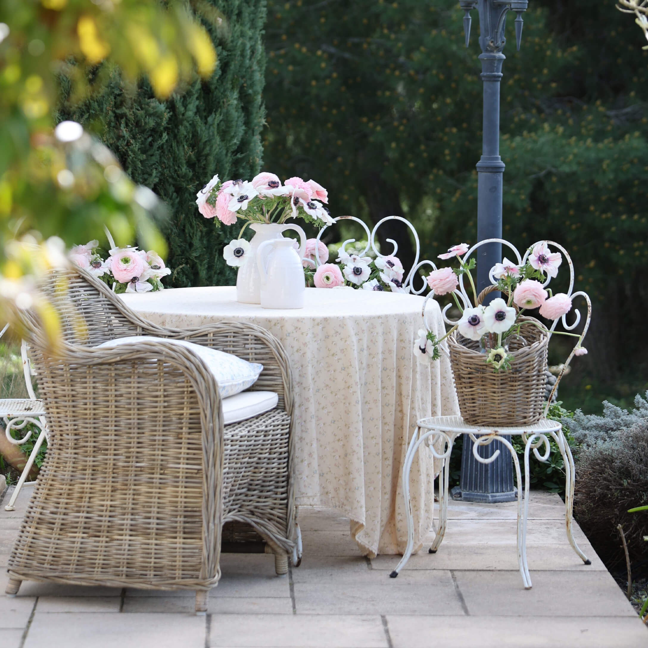 Tuin met rotan stoel, witte tafel met tafelkleed en bloemen in vazen, romantische sfeer