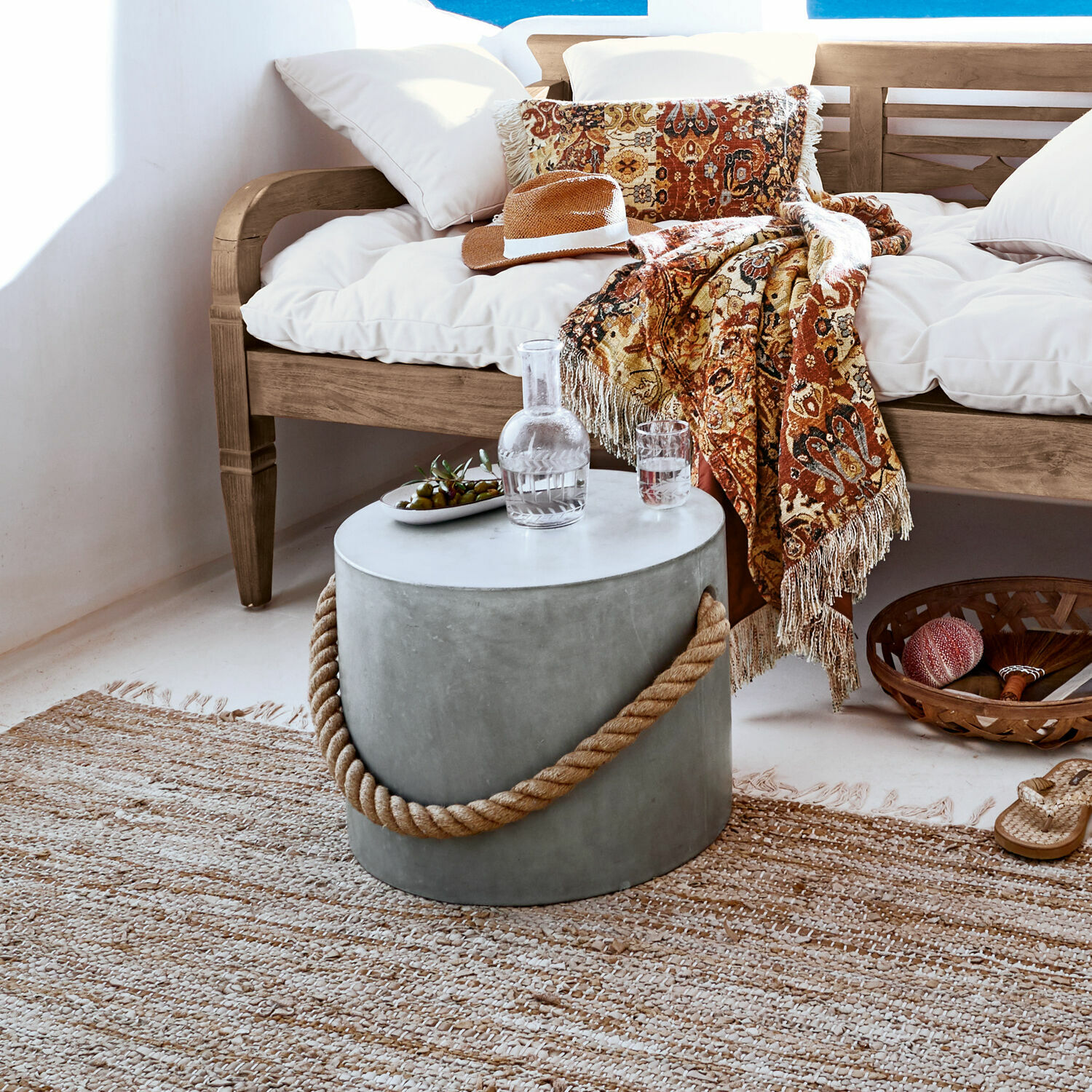 Ronde betonnen bijzettafel met touwhandvat in natuurlijke woonkamer met houten bank en decoratief plaid