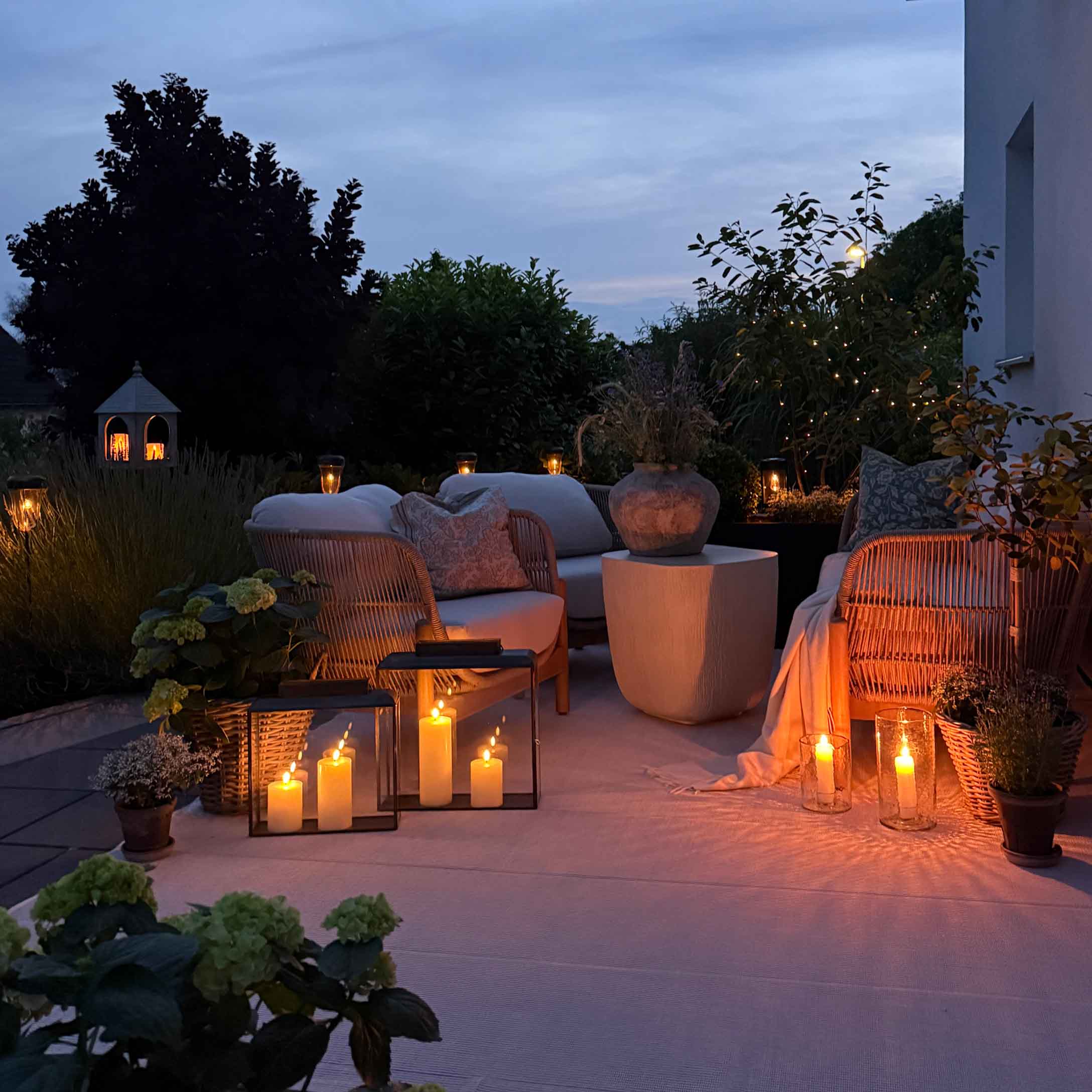 Gezellige tuin met witte kussens op meubels en decoratieve kaarsen buiten in de avond