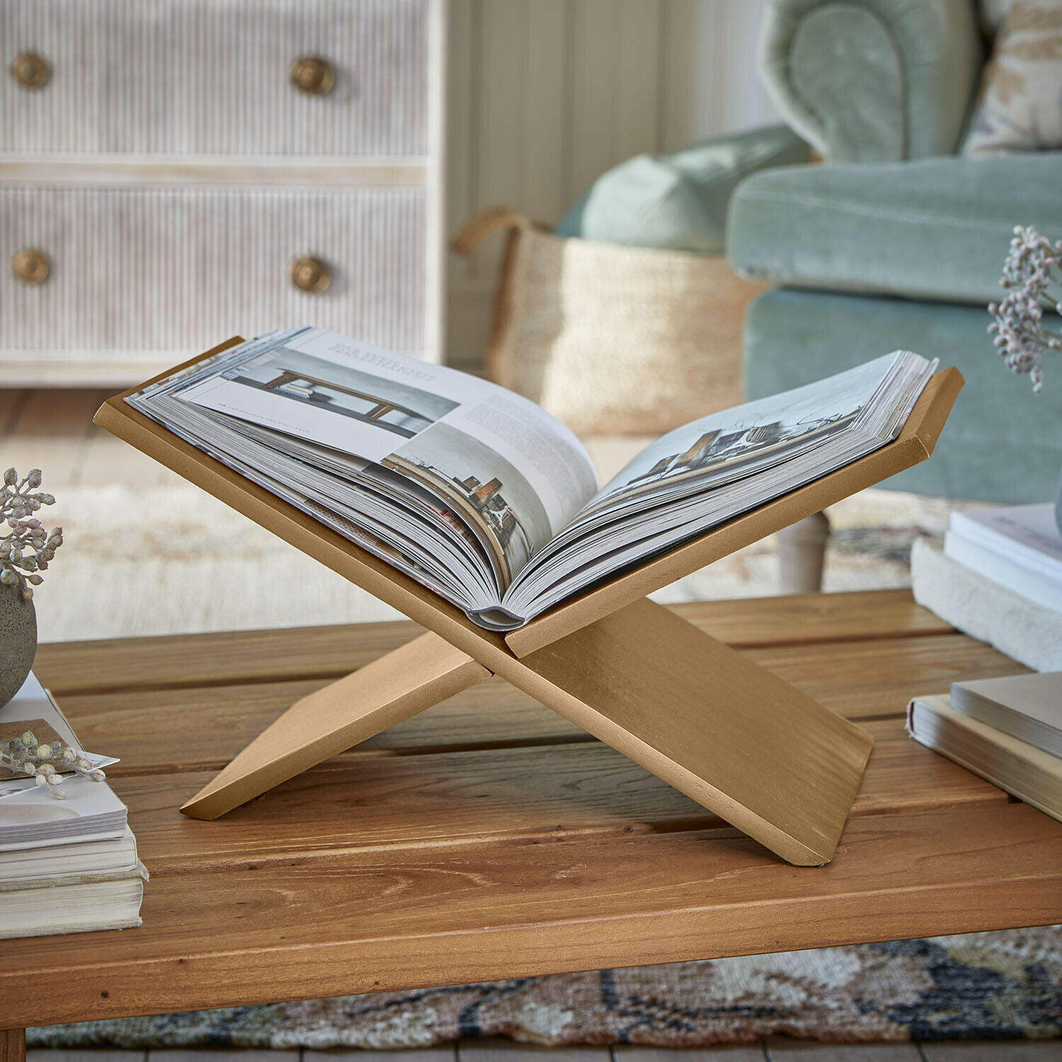 Gouden houten boekenstandaard op salontafel in gezellige woonkamer met groene bank