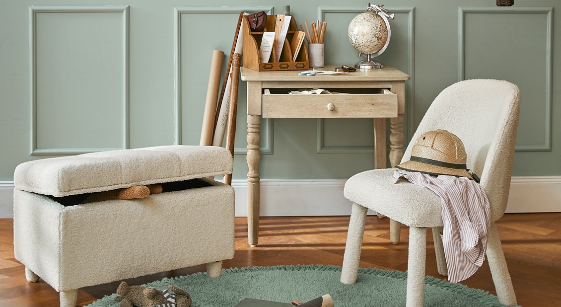 Gezellige kamer met crème bouclé stoel en poef, lichte houten tafel en decoratieve wereldbol