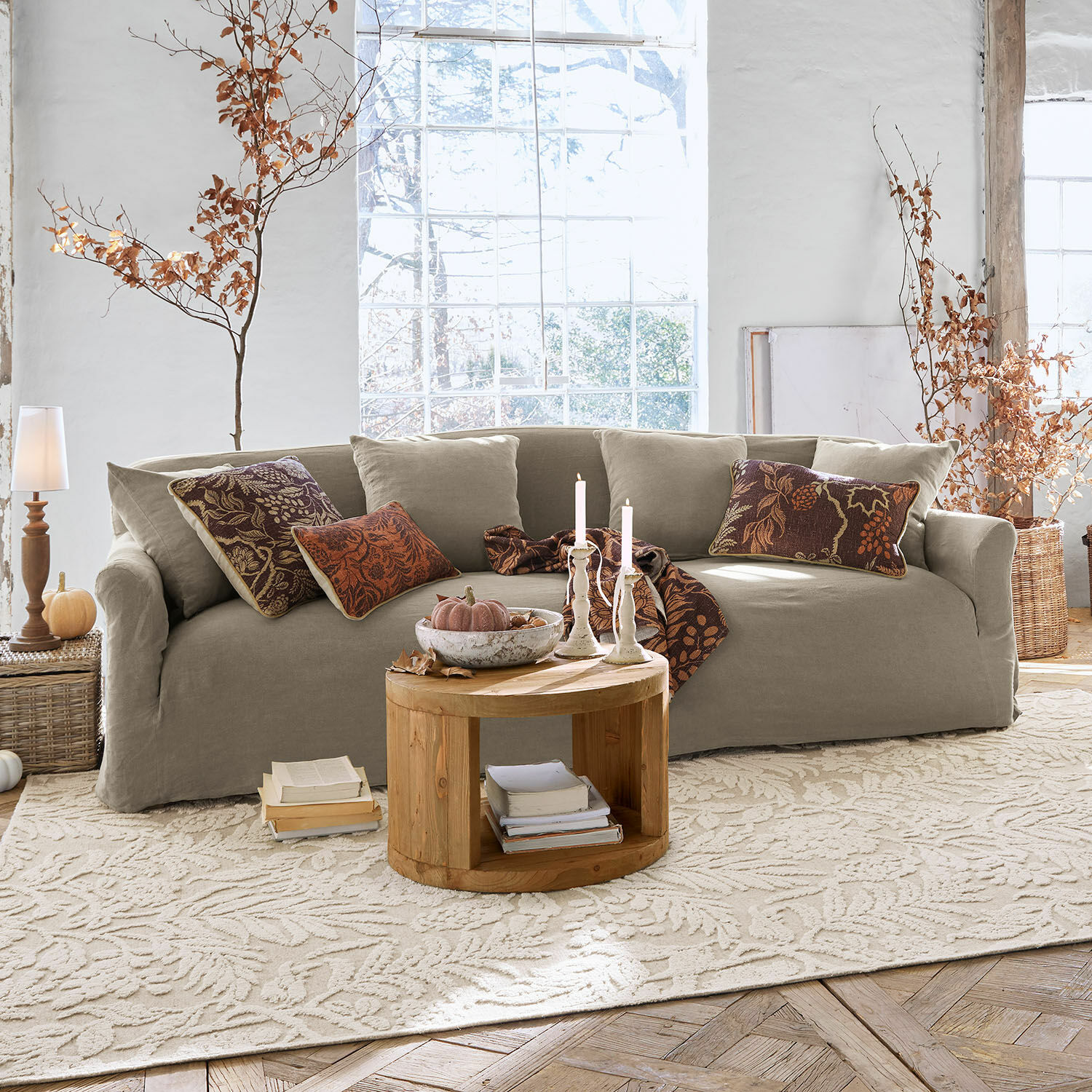 Bank Riveneuve Beige stoffen bank in lichte woonkamer met ronde houten tafel en herfstdecoratie