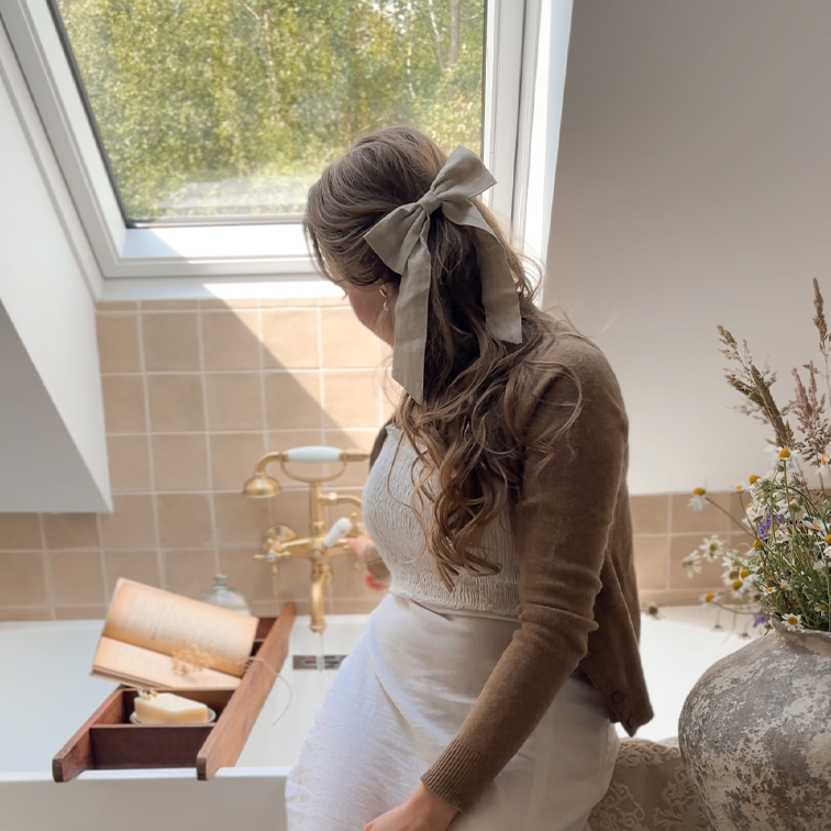 Vrouw met beige linnen strik in haar zittend bij bad met houten plank en boek, natuurlijk licht