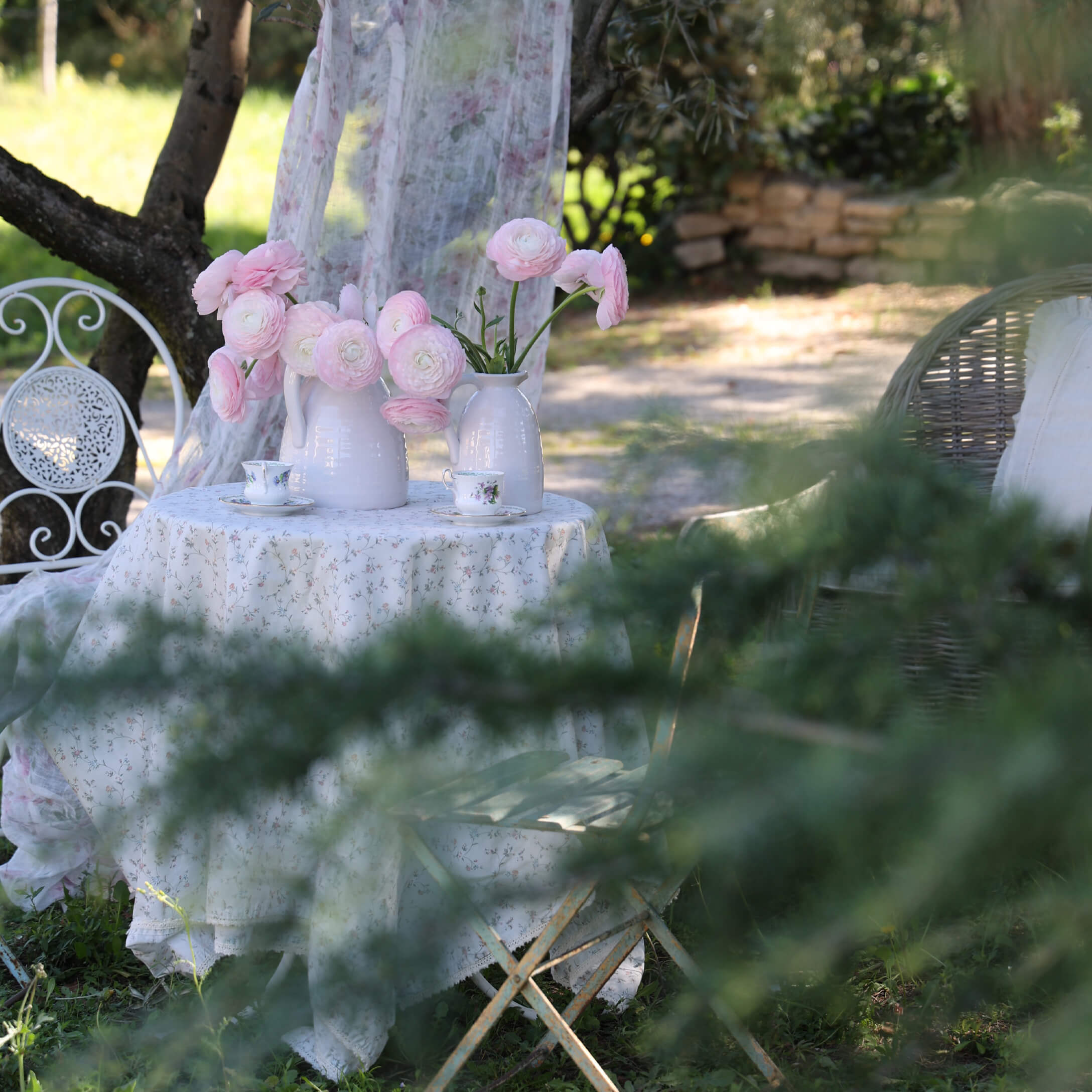 Witte tuintafel met bloemen tafelkleed en witte vazen met roze bloemen, romantische setting