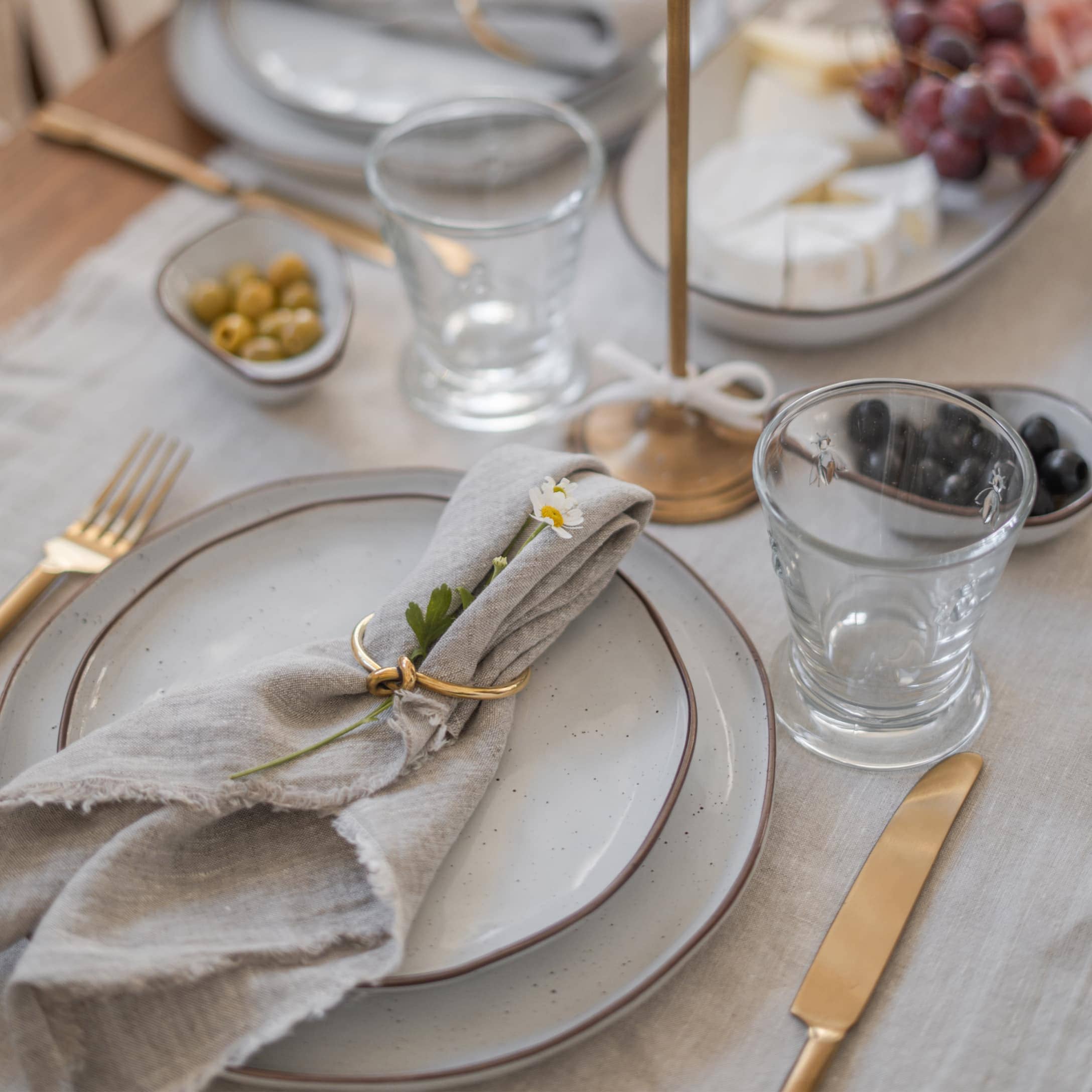 Elegante tafelsetting met grijze borden, gouden bestek en linnen servet met bloem