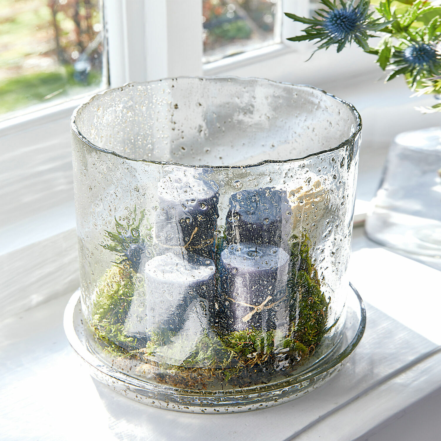 Glazen windlicht met luchtbellen en zwarte kaarsen op groen mos op vensterbank