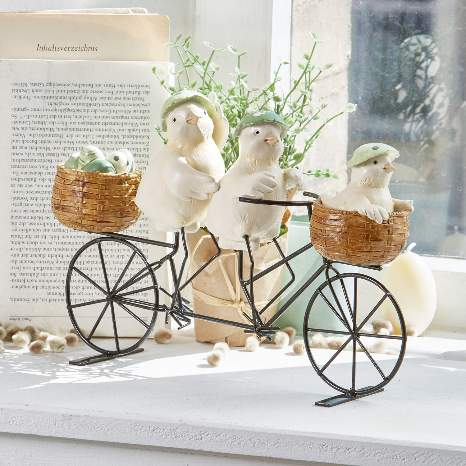 Decoratie met drie witte vogeltjes met groene hoedjes op metalen fiets met rieten manden