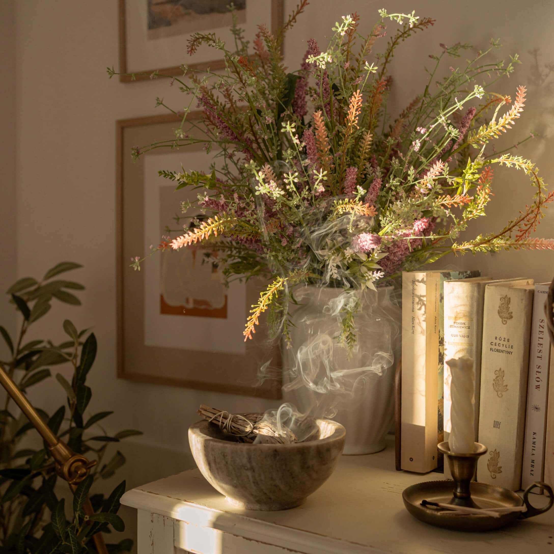 Alabaster kom met rokende salie naast vaas met kleurrijke bloemen en boeken op tafel