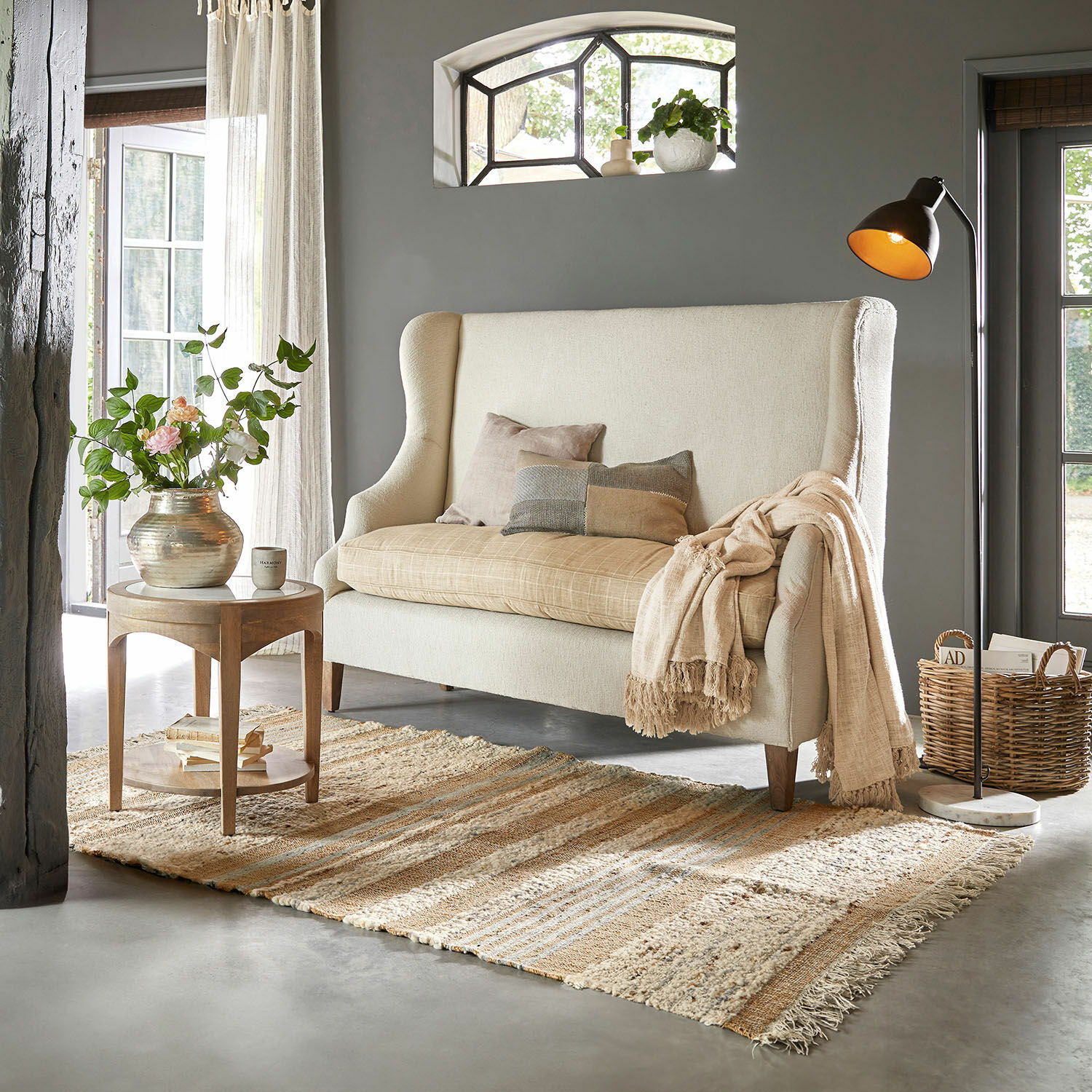 Beige bank met hoge rugleuning en kussens in gezellige woonkamer met vloerkleed en staande lamp