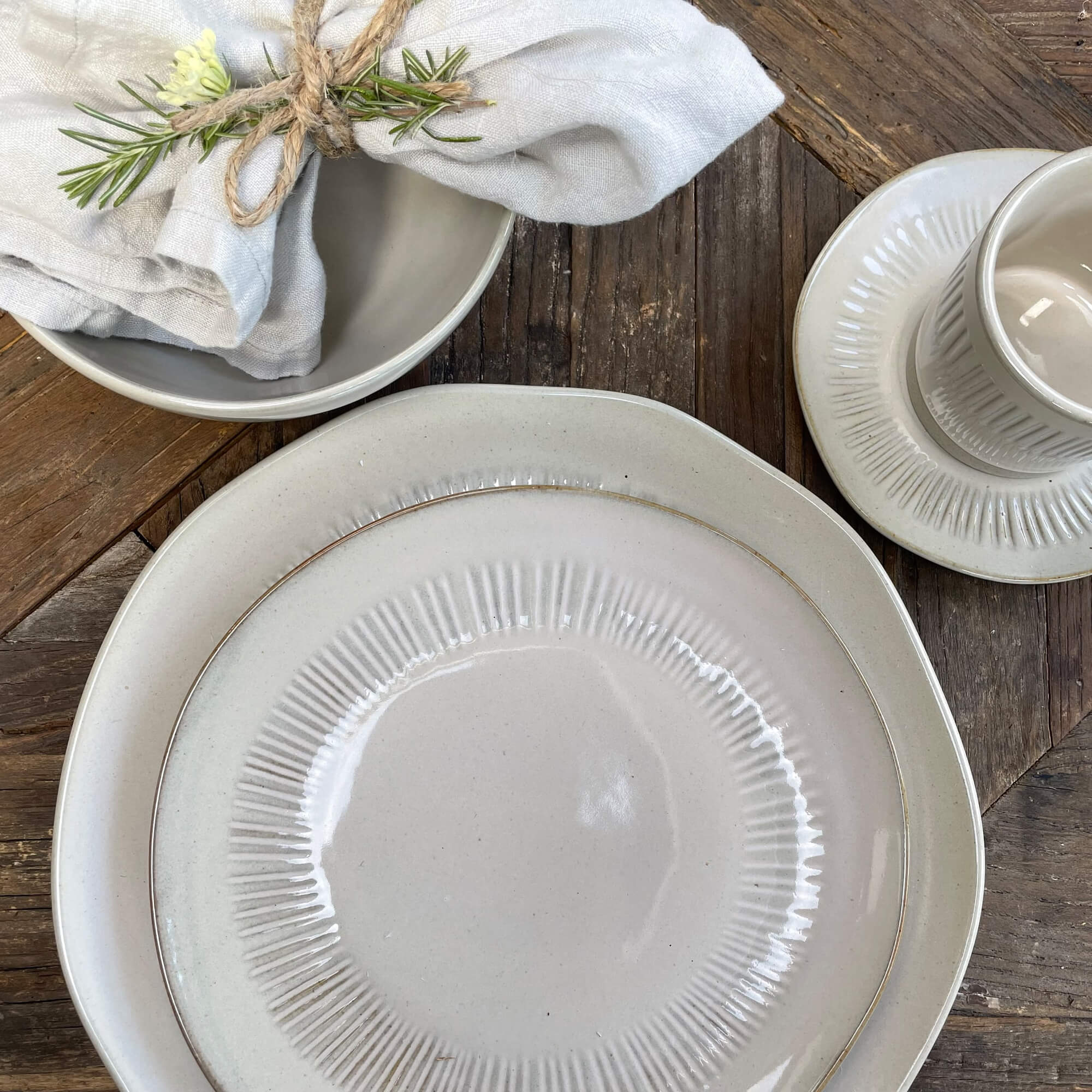 Set licht keramisch servies met borden en kopje op houten tafel, linnen servet met rozemarijn