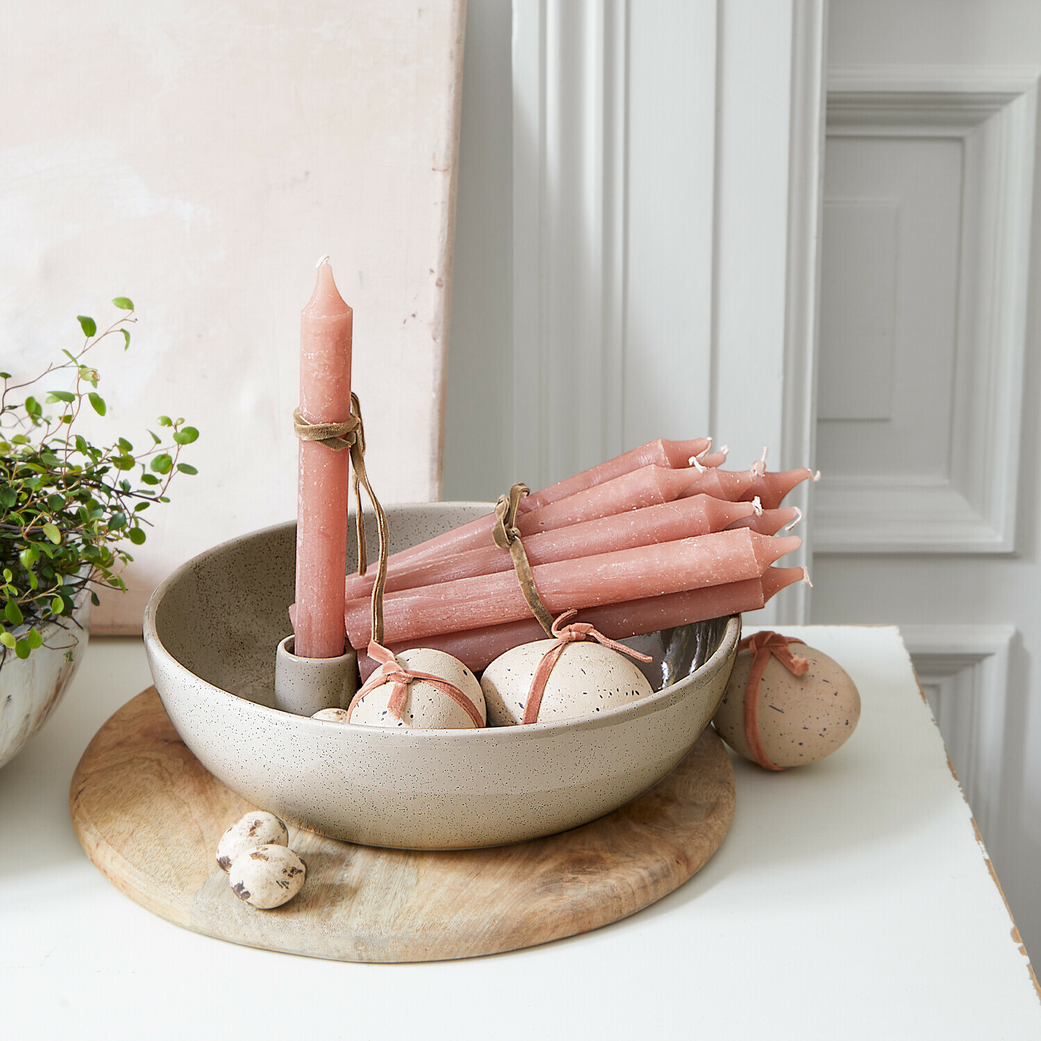 Set roze dinerkaarsen en decoratieve eieren in keramische schaal op houten onderzetter