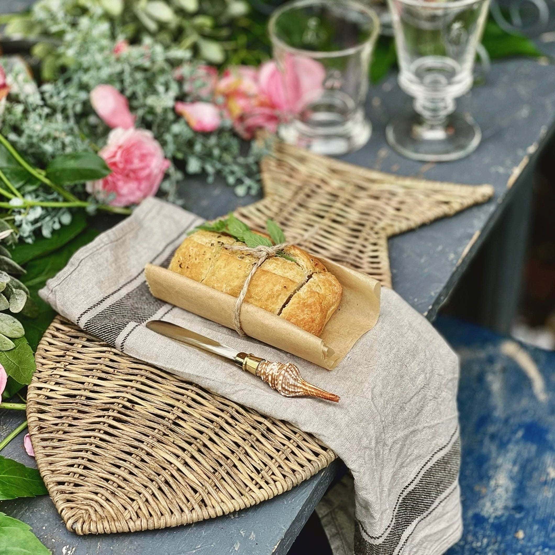 Rustieke gevlochten placemat van zeegras met brood en schelphandvatmes op oude tafel