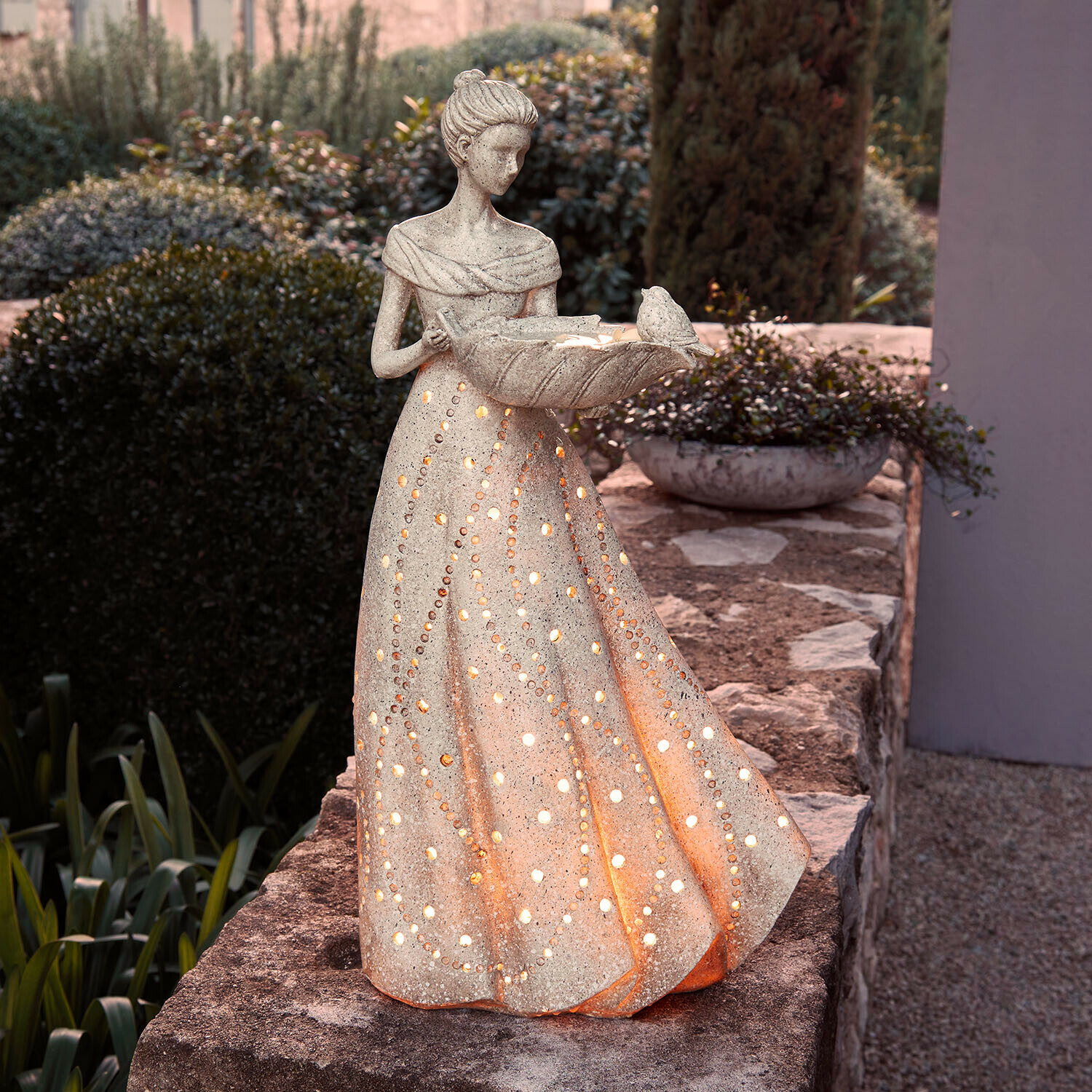 Verlichte stenen beeld van vrouw in jurk met gaten, tuindecoratie met vogel
