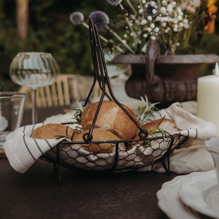 Metalen broodmand met handvatten, bekleed met linnen doek, gevuld met broodjes en kruiden op tafel