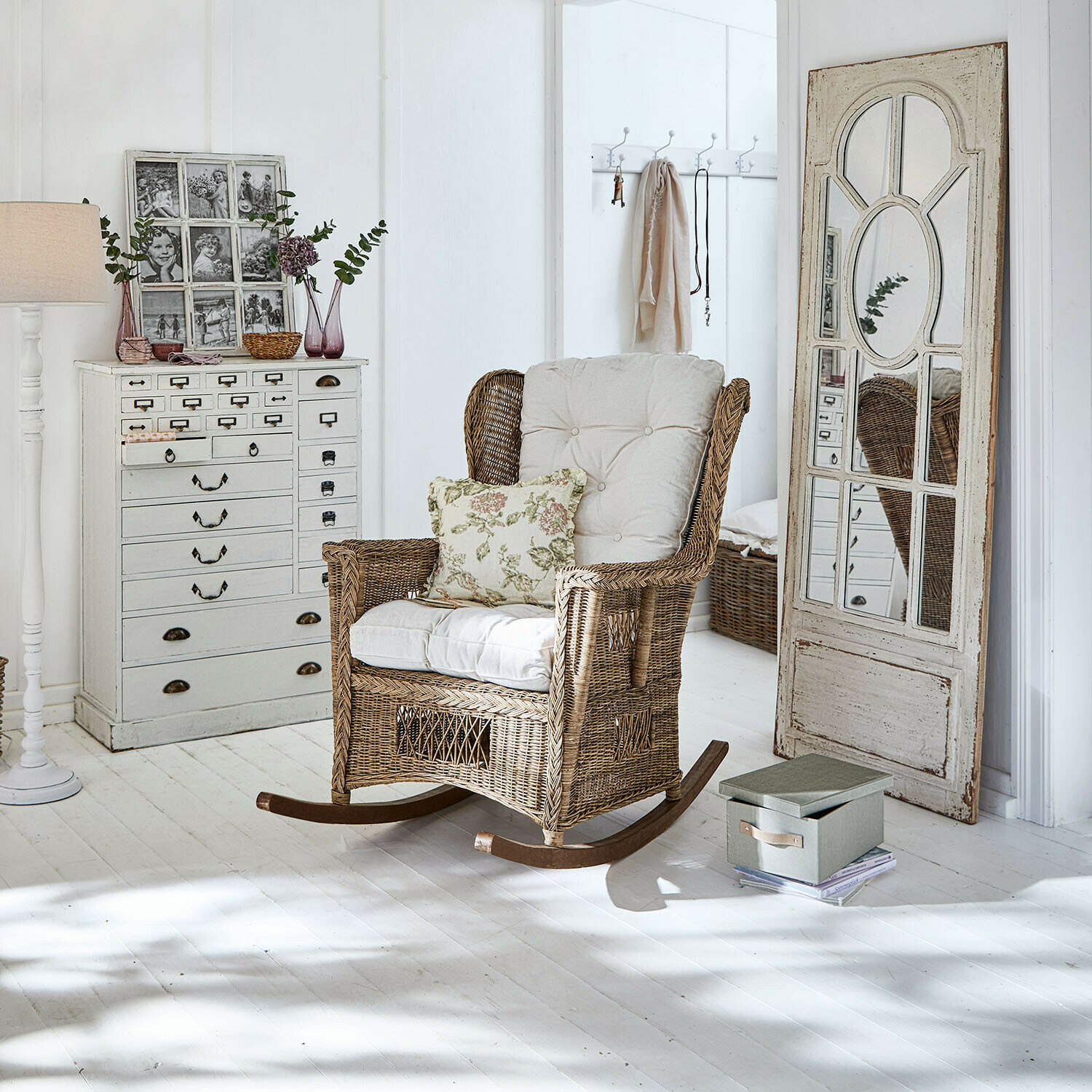 Schommelstoel van riet met crèmekleurige kussens in lichte kamer met witte vloer