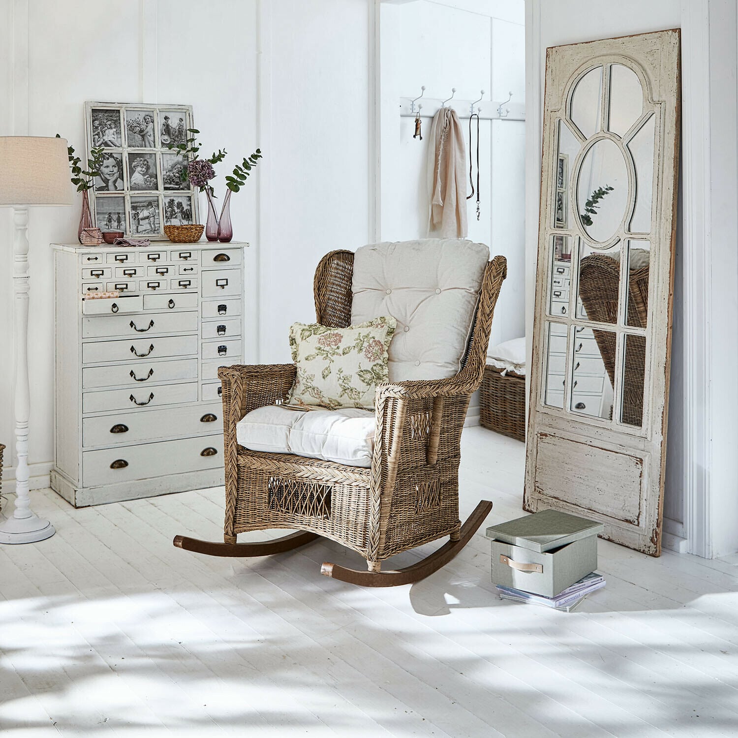 Schommelstoel Jeveren Schommelstoel van riet met crèmekleurige kussens in lichte kamer met witte vloer
