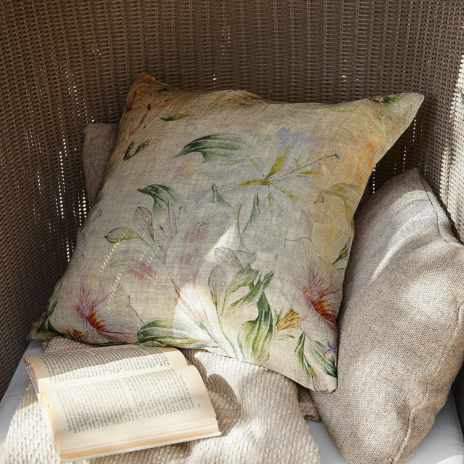 Decoratief linnen kussen met bloemenpatroon in natuurlijke kleuren op rotan stoel