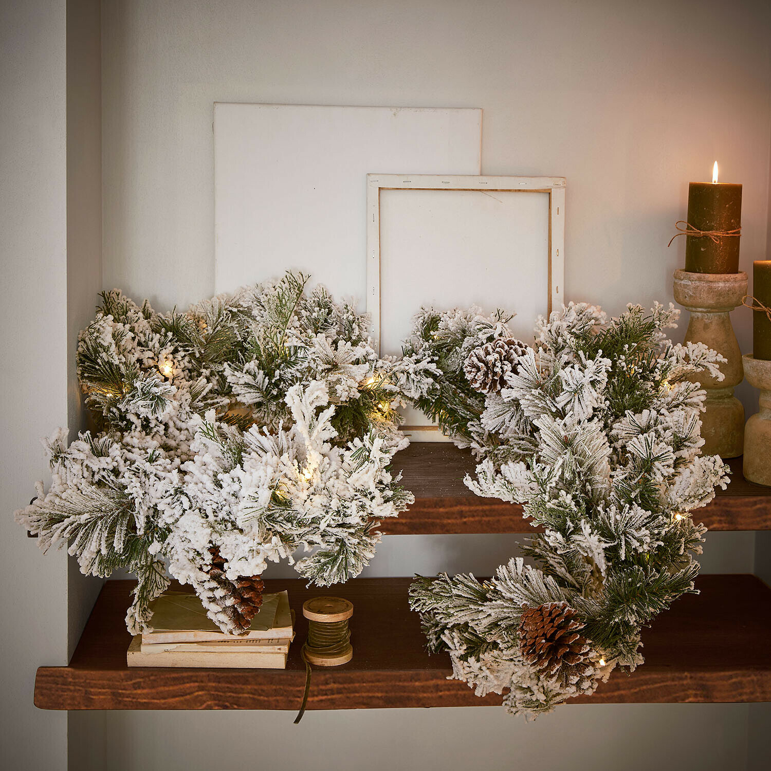 Kerstkrans van groene takken met kunstsneeuw en dennenappels met LED-lichtjes op houten plank