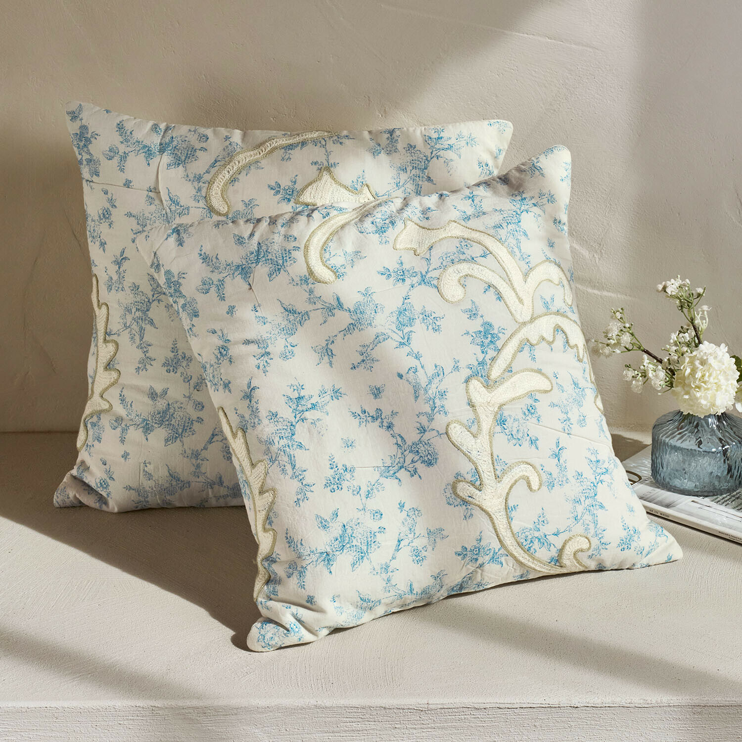 Twee decoratieve katoenen kussens in crème met blauw bloemenpatroon en fijne borduursels