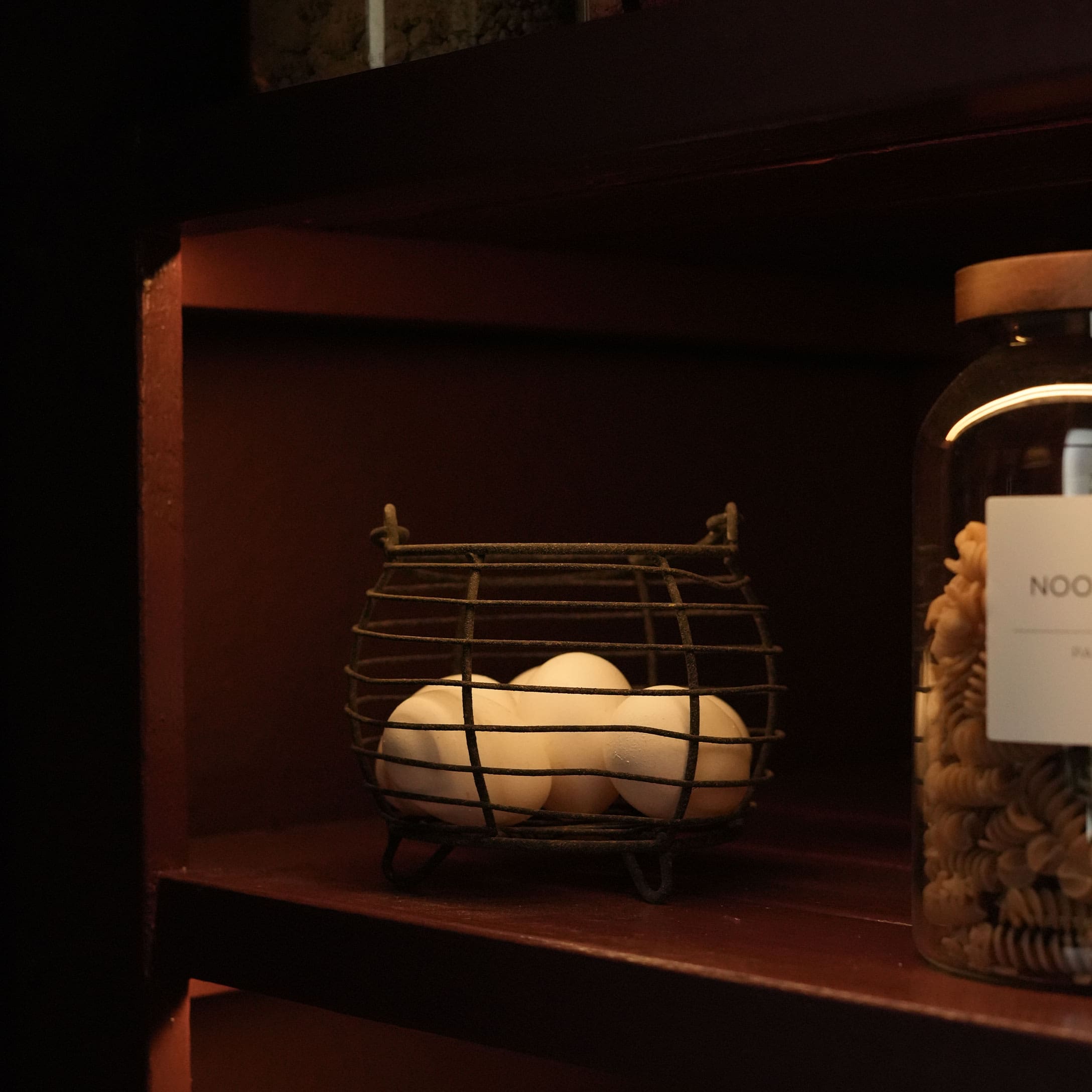 Metalen mand met witte eieren op een donkere houten plank in een rustiek interieur