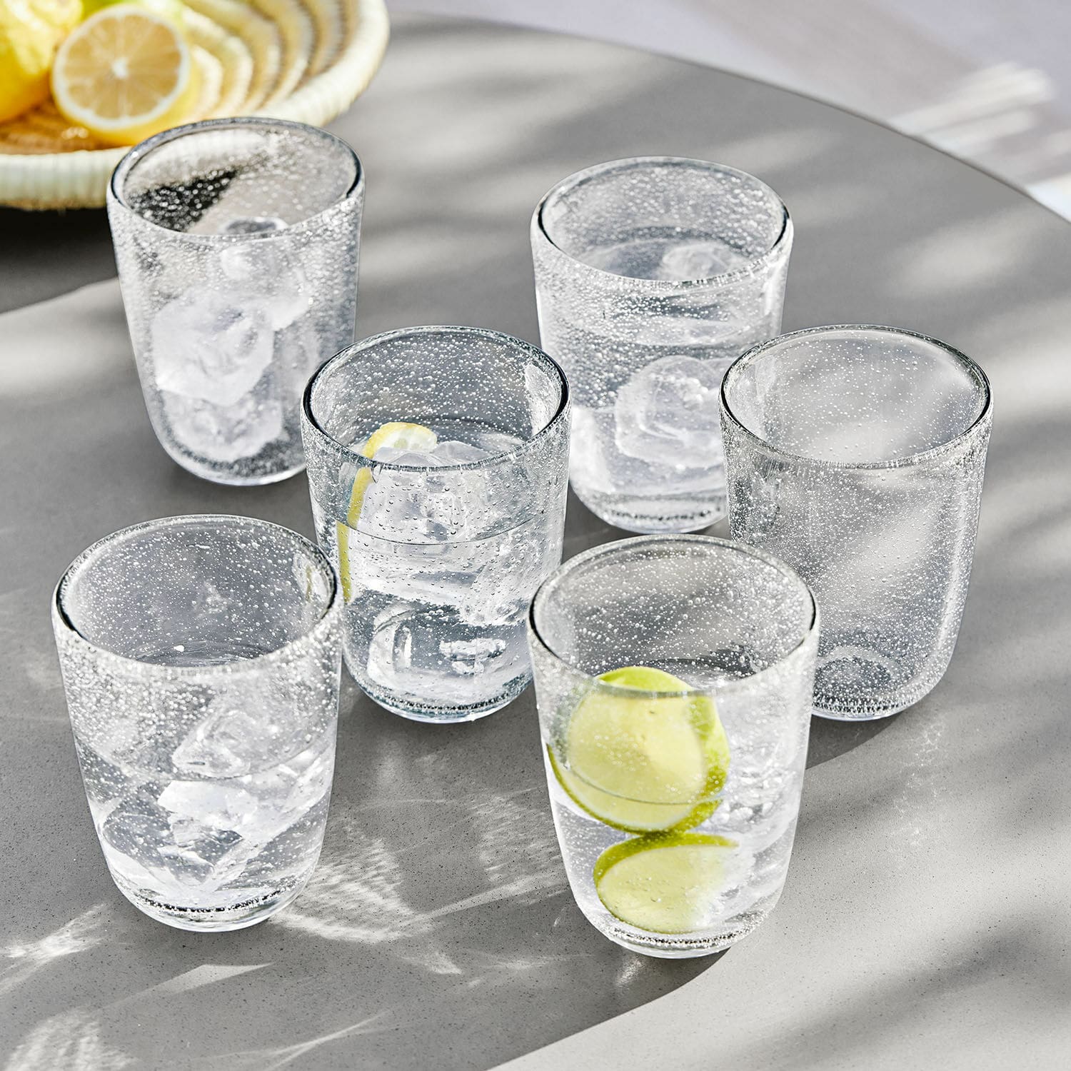 Glas set van 6 Parilly Set van zes transparante bubbeltjesglazen met ijsblokjes en citroenschijfjes op een grijze tafel