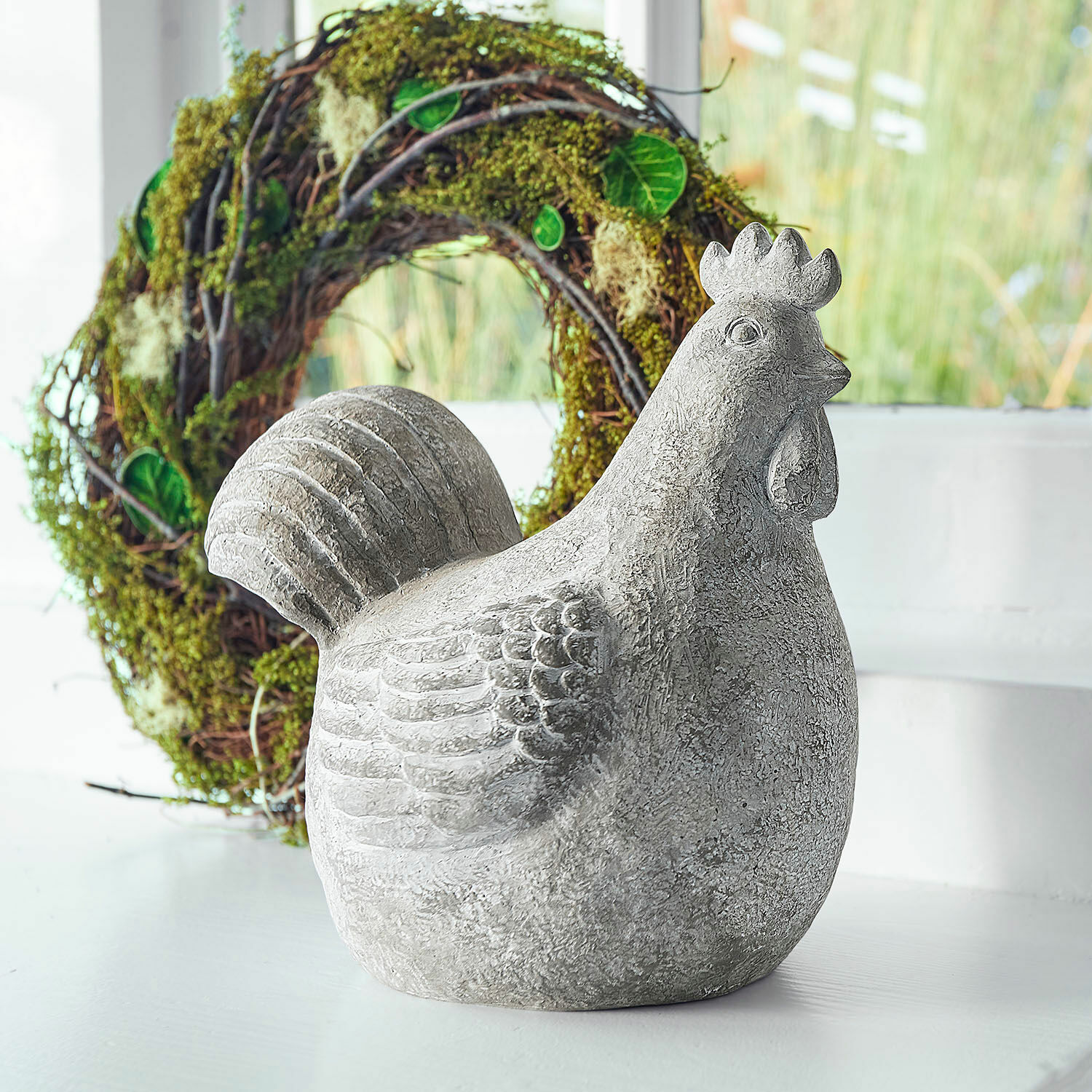 Decoratieve kip Roselique Grijs betonnen kippenbeeld als decoratie op lichte achtergrond met groene krans op de achtergrond