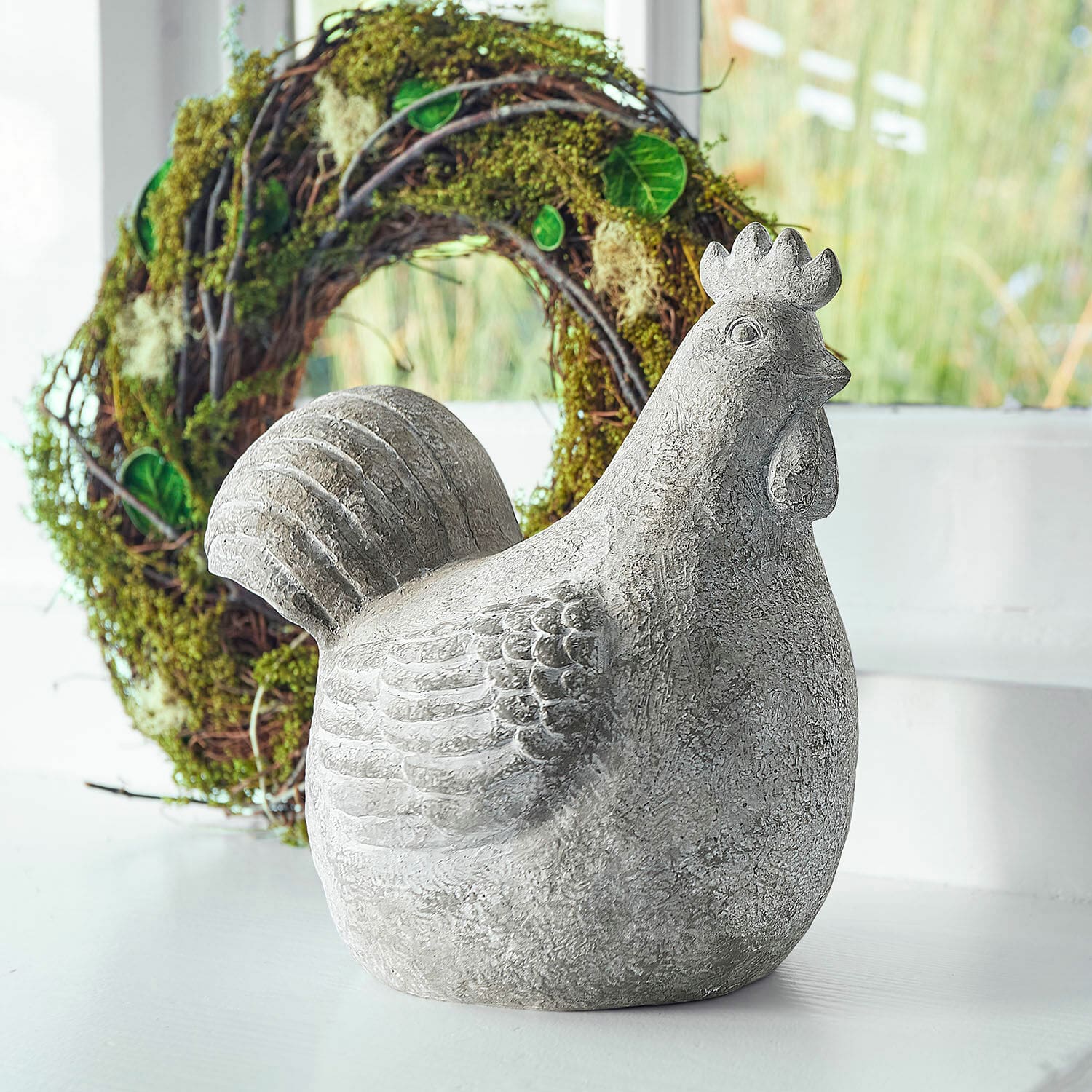 Decoratieve kip Roselique Grijs betonnen kippenbeeld als decoratie op lichte achtergrond met groene krans op de achtergrond