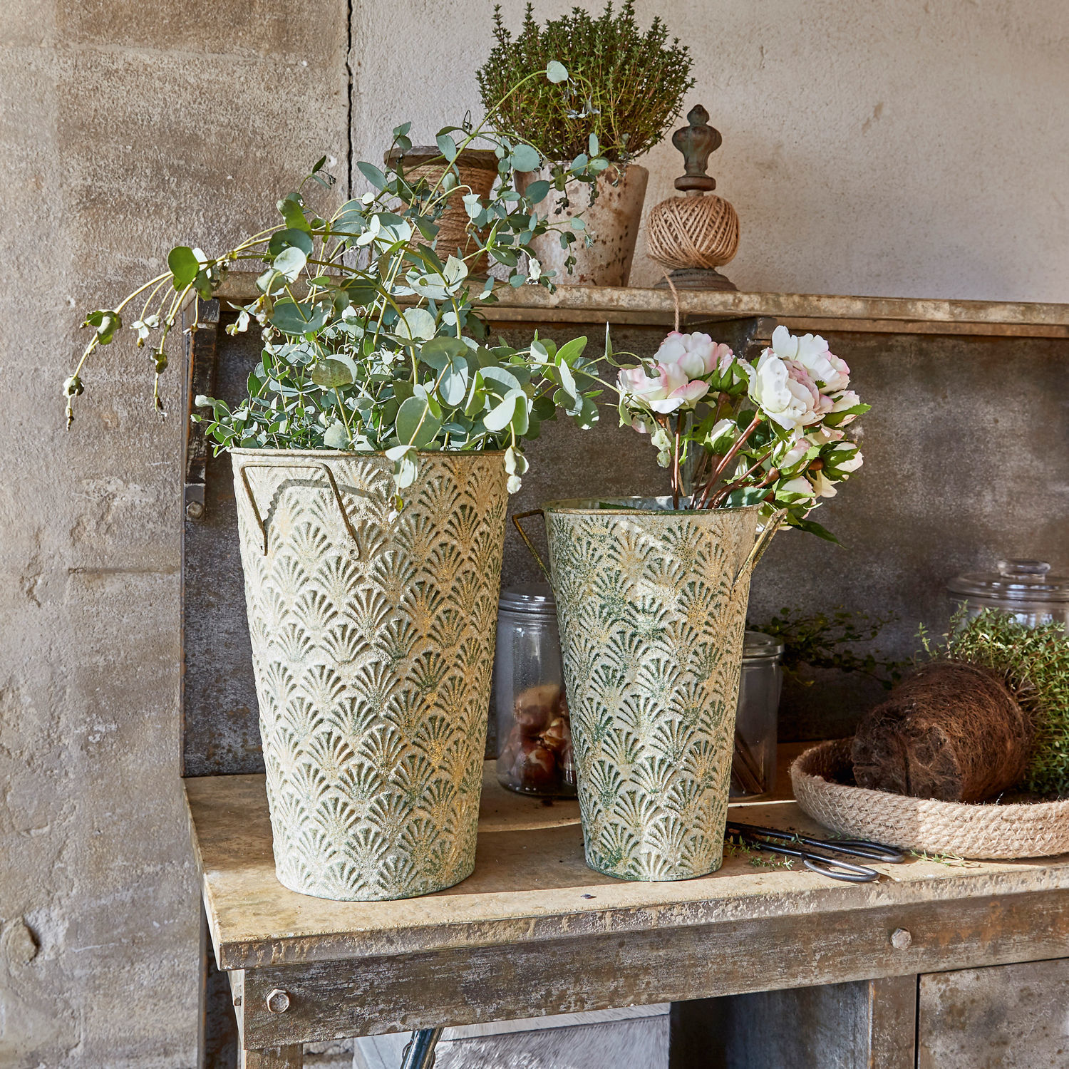 Twee decoratieve metalen bloempotten in groen-beige met planten op rustieke houten tafel