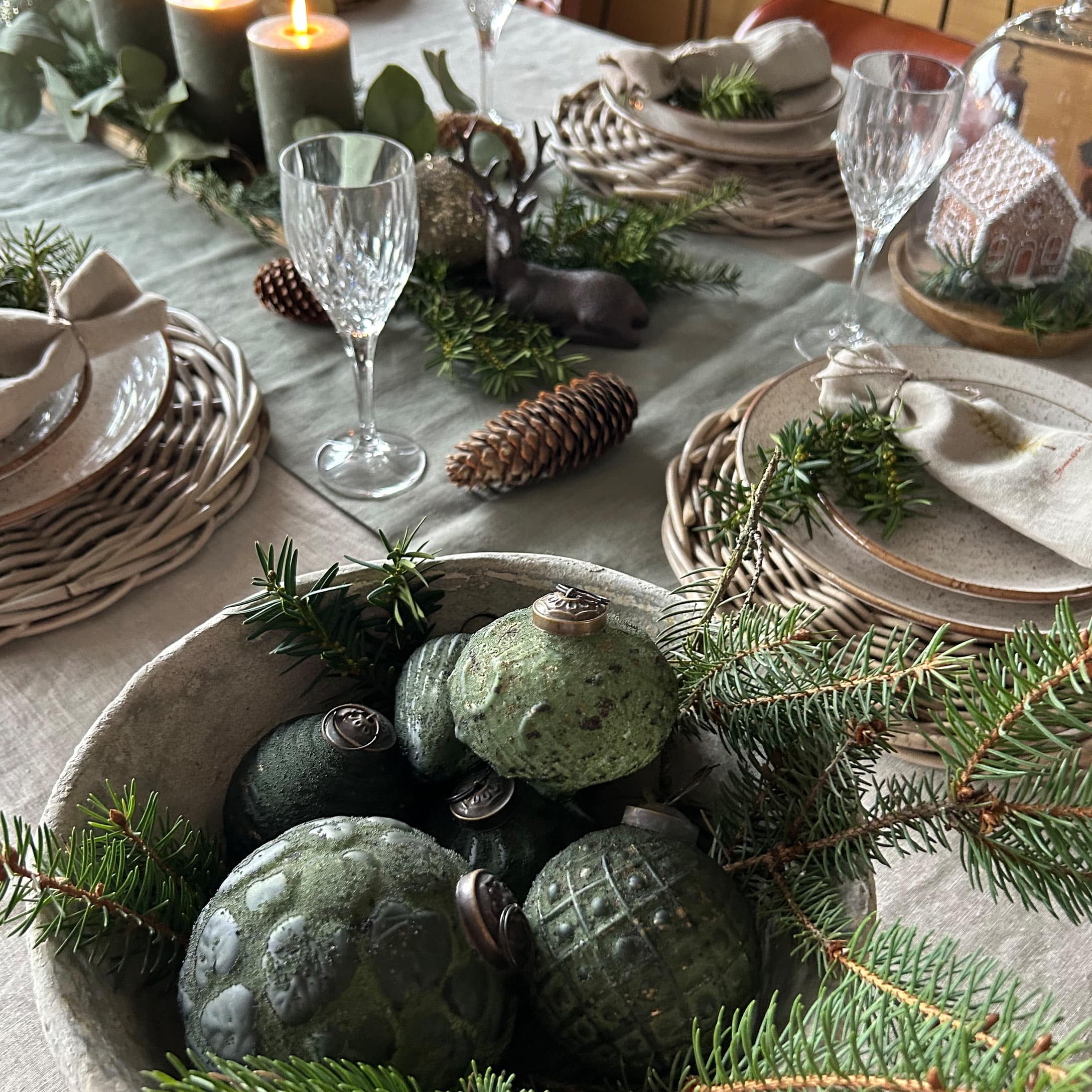Groene keramische kerstballen in schaal met dennentakken op feestelijk gedekte tafel