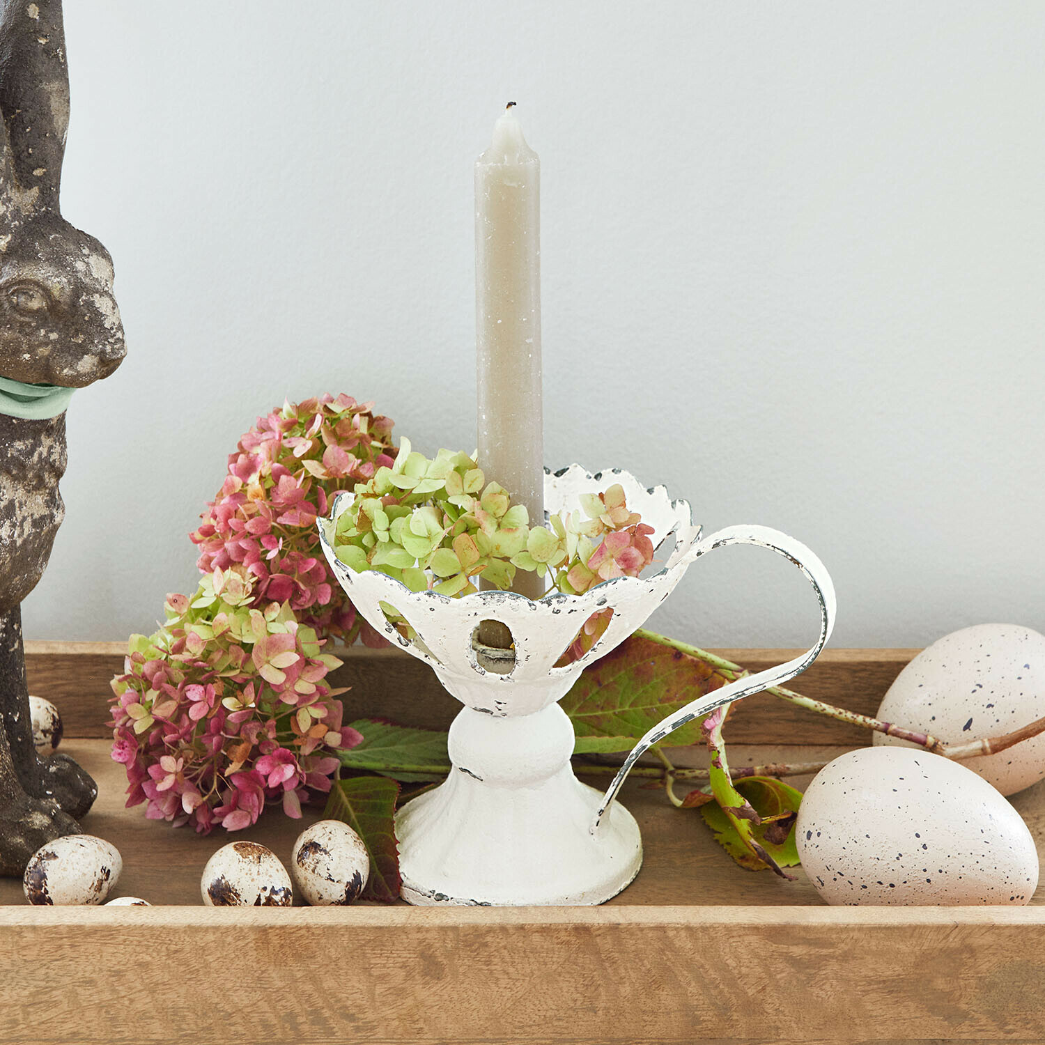 Witte metalen kandelaar met handvat en grijze kaars, versierd met bloemen en decoratieve eieren