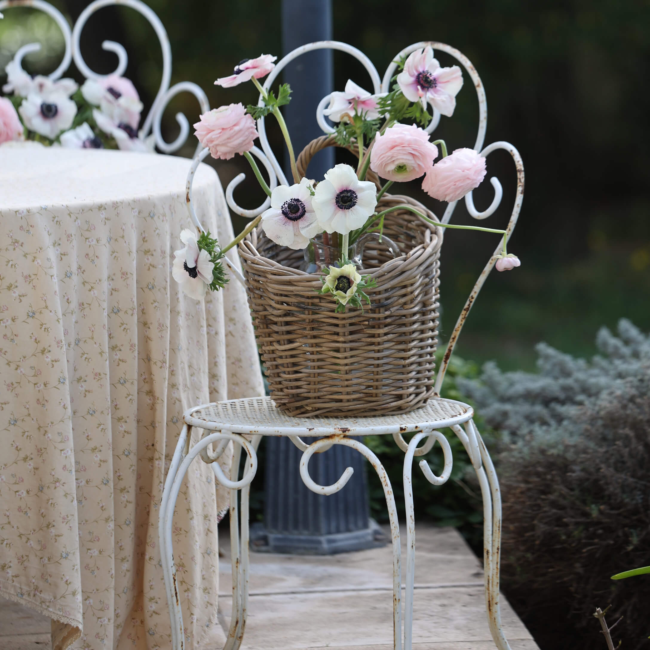 Rieten mand met roze en witte bloemen op witte metalen stoel in tuin